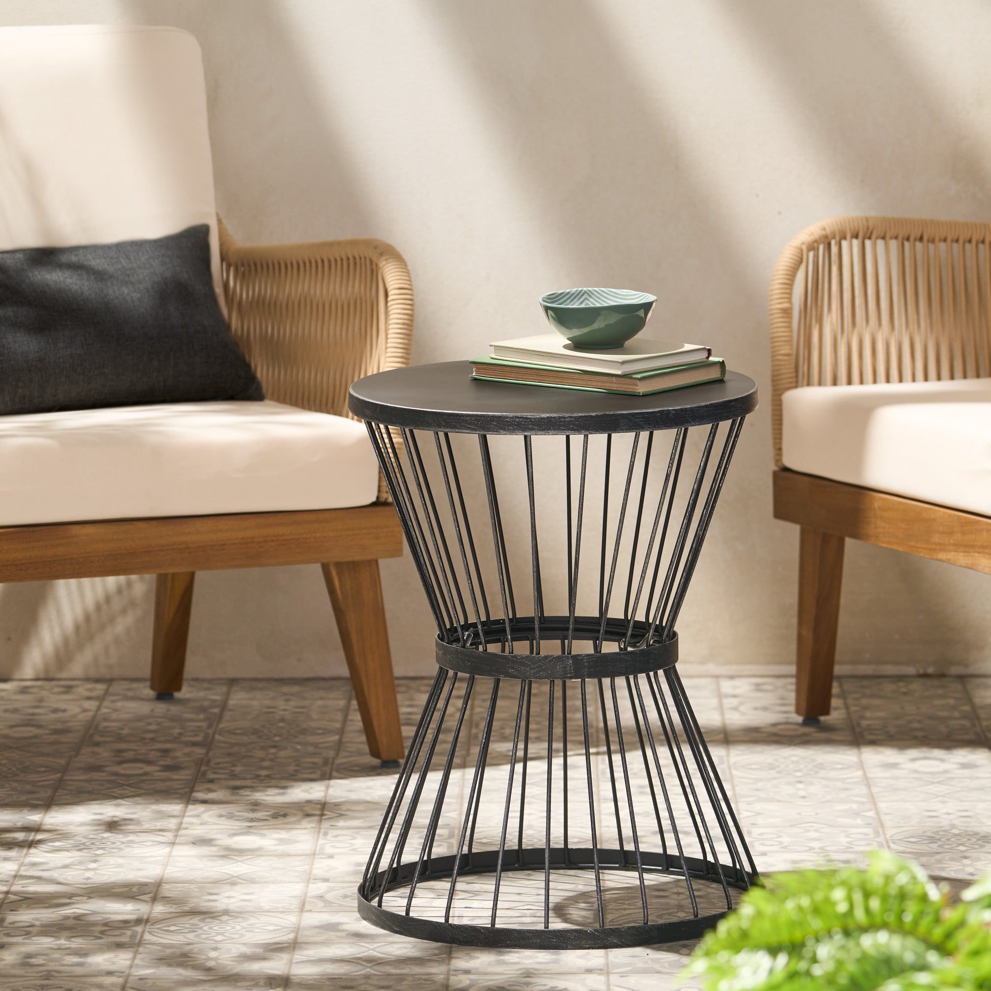 Black metal wire hourglass side table with weathered finish holding books and a bowl