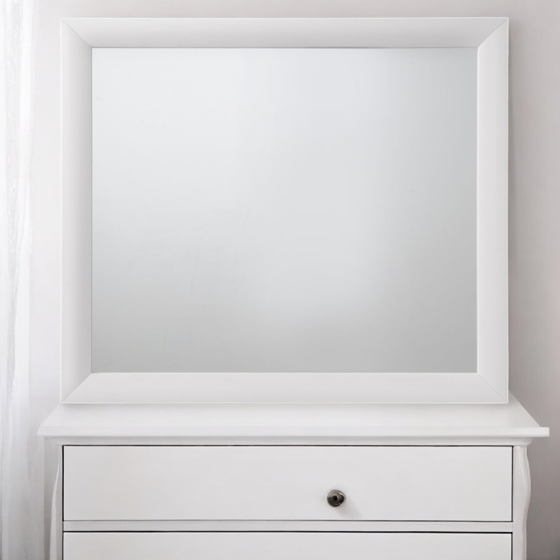 White framed vanity mirror atop a white dresser