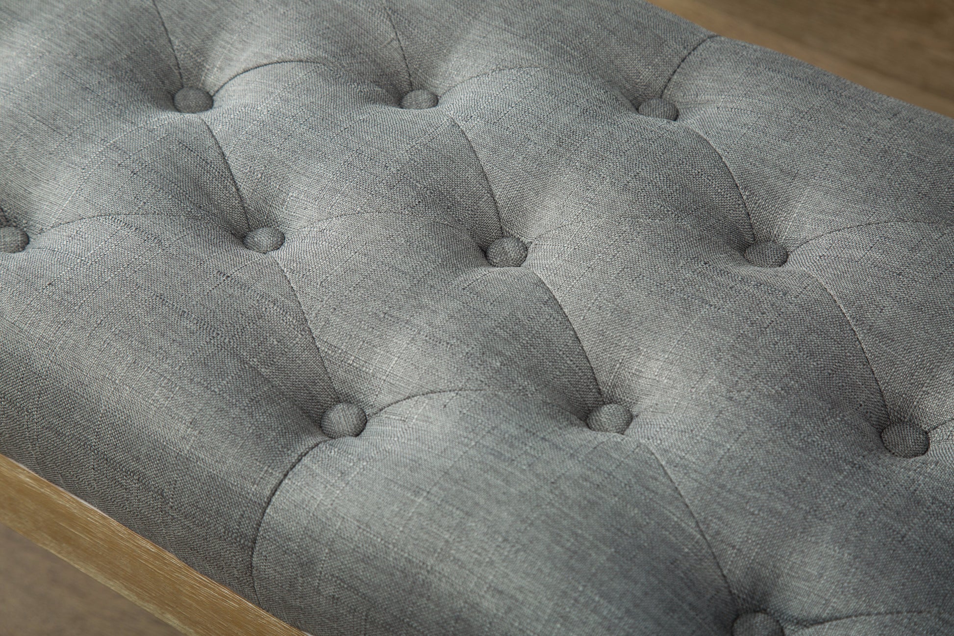 Gray tufted fabric ottoman with natural wood frame detail
