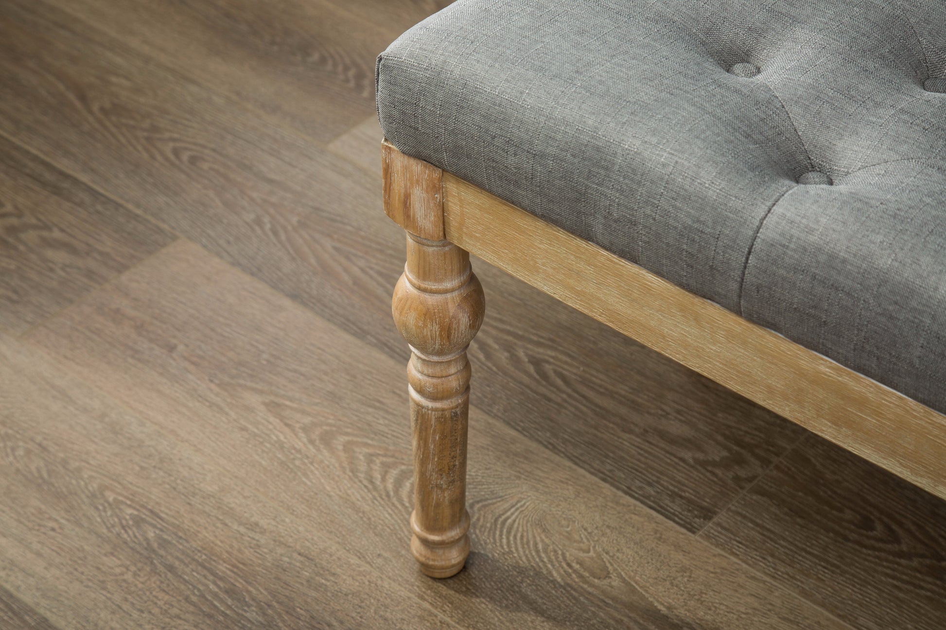 Tufted grey linen bench with ornate wooden leg detail