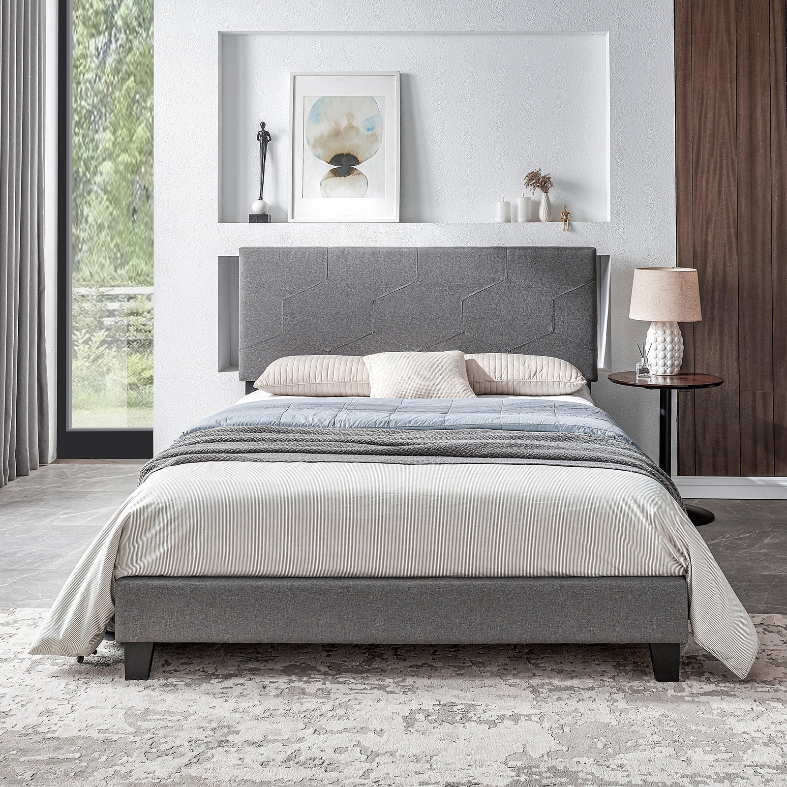 Grey upholstered bed frame with geometric headboard and striped duvet