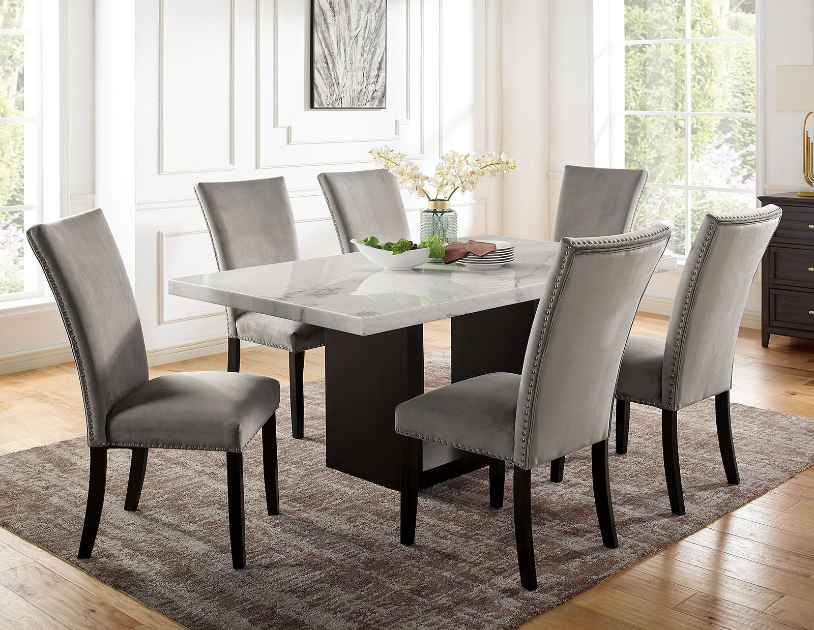 Gray velvet dining chairs with silver nailhead trim around marbletop table