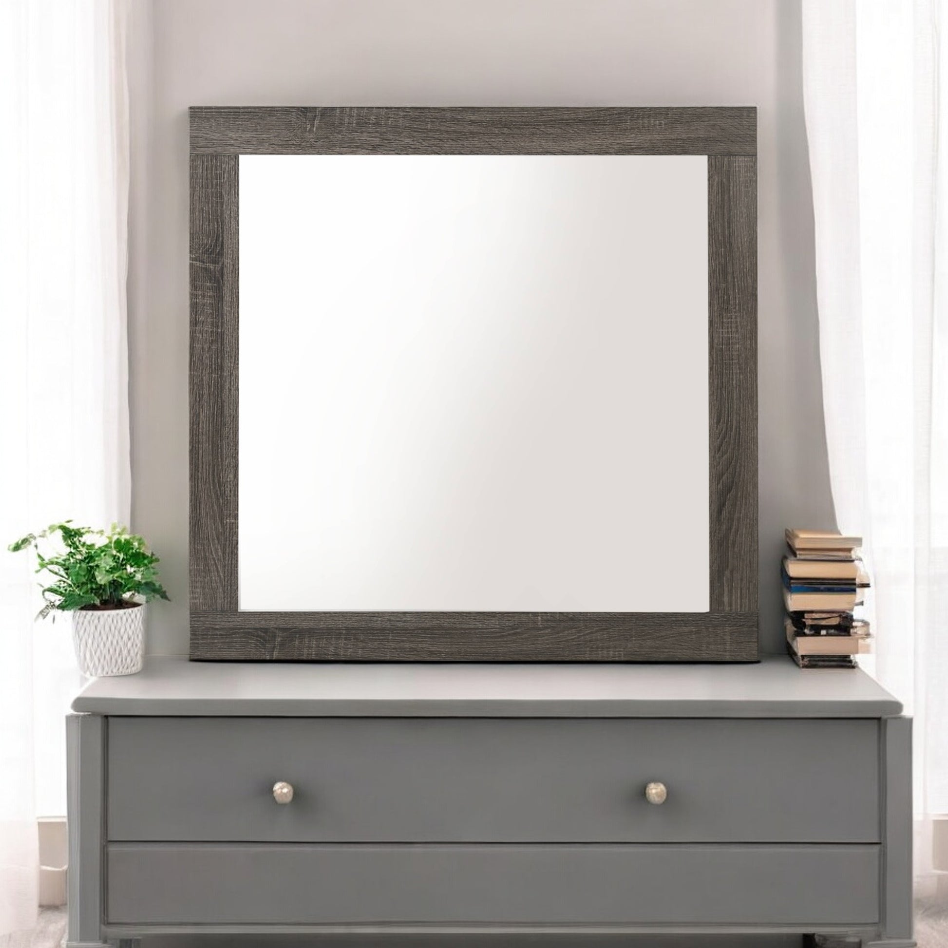 Rustic wood framed mirror mounted on a grey dresser with decorative plants and books
