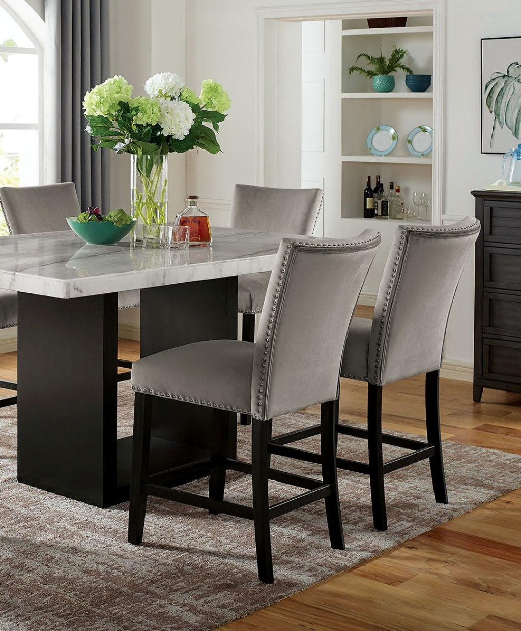 Plush grey velvet bar stools with silver nailhead trim around a marbletop dining table