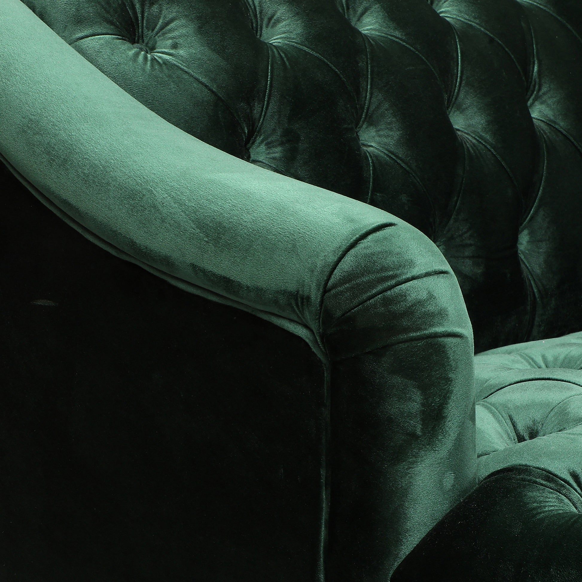 Deep emerald green velvet armchair with tufted detailing and a rolled armrest