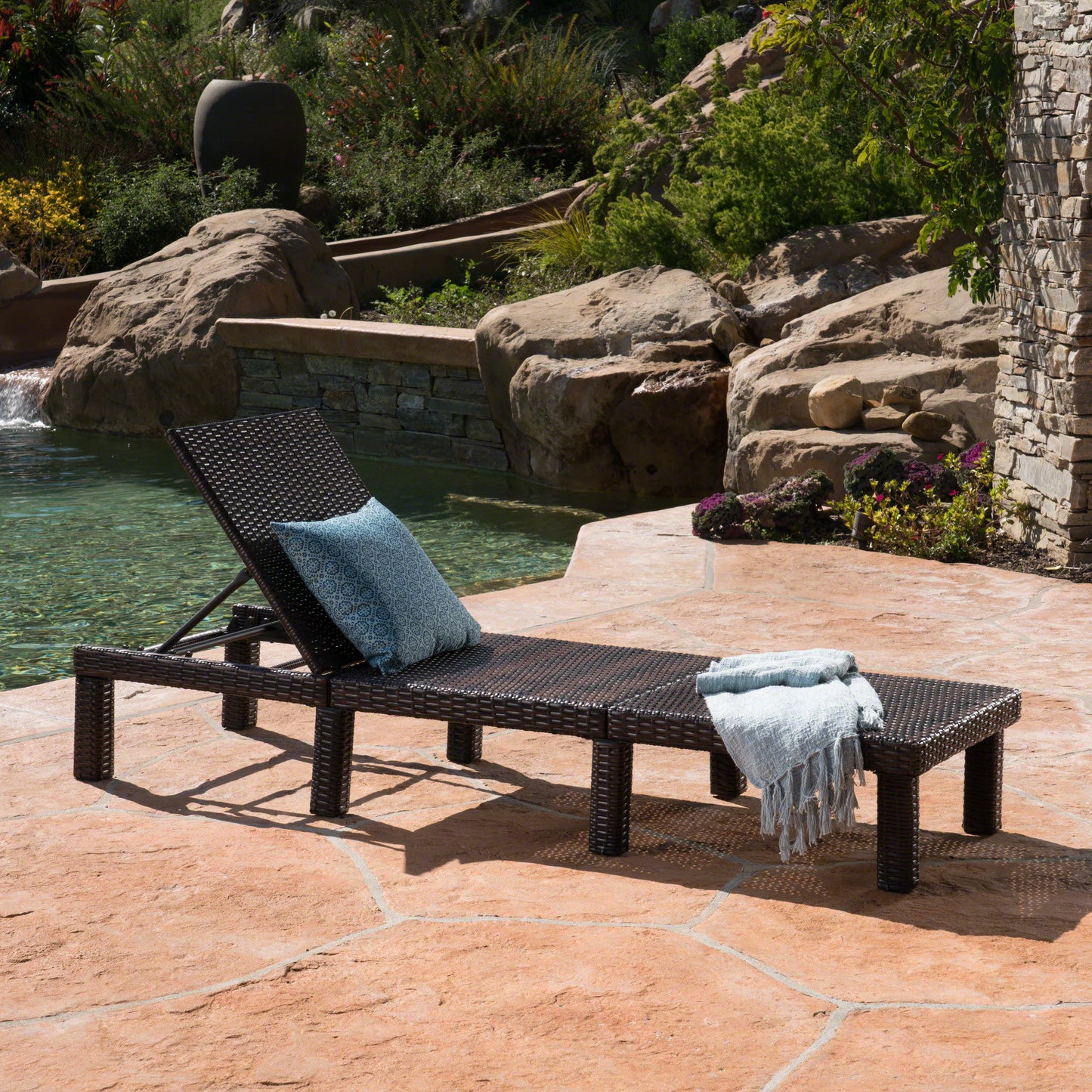 Dark brown rattan chaise lounge chair with blue patterned cushion by pool