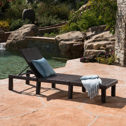 Dark brown rattan chaise lounge chair with blue patterned cushion by pool