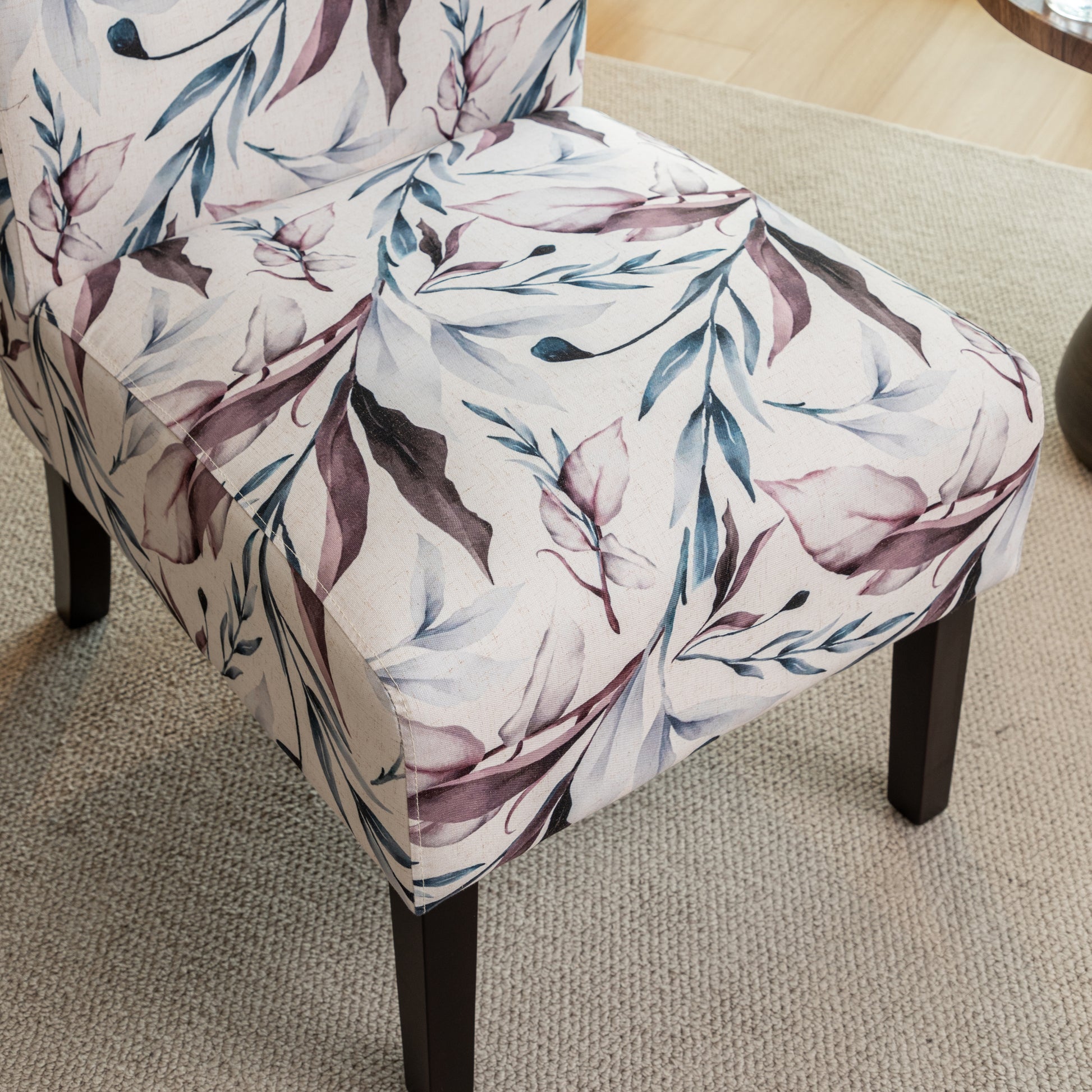 Upholstered accent chair with a watercolor botanical leaf print in blush and teal on a neutral background