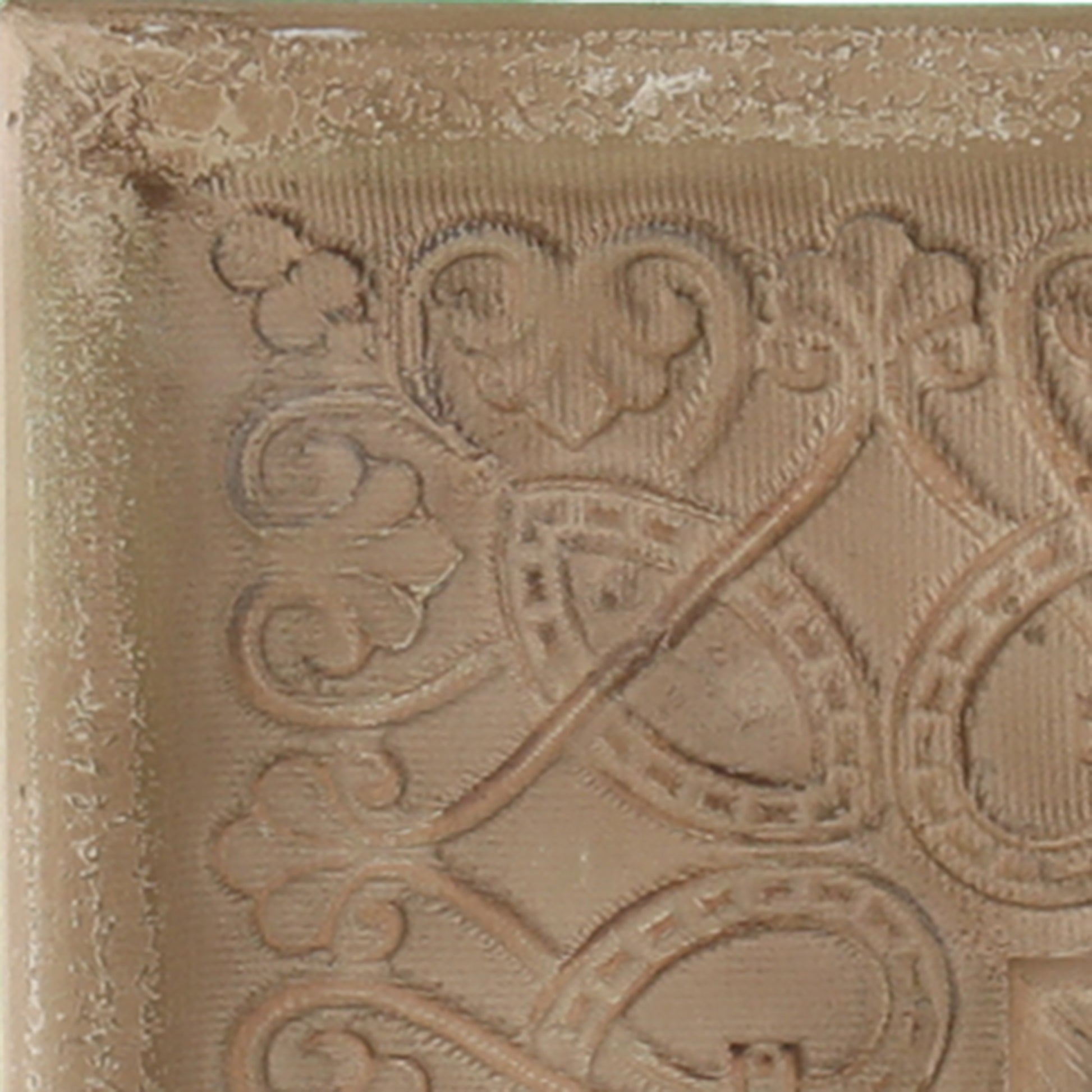 Closeup of a tan ceramic tile with ornate embossed scrollwork pattern x inches