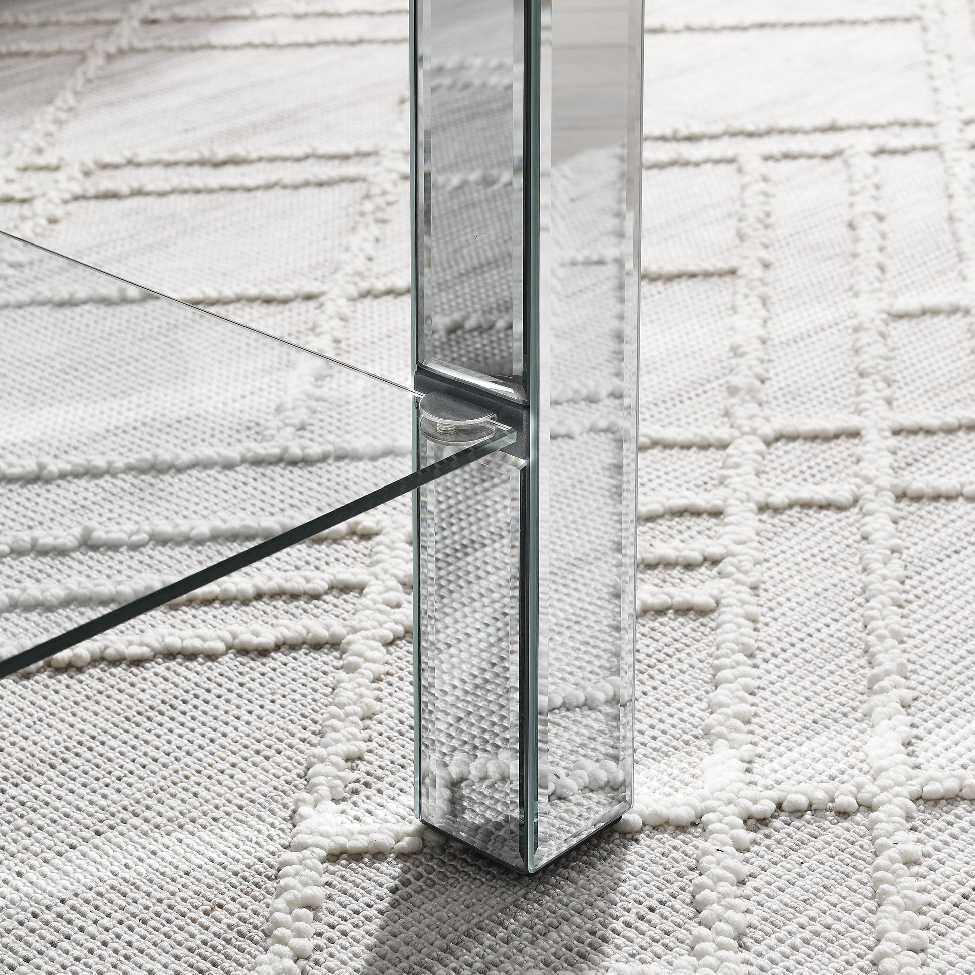 Closeup of a clear glass table leg with mirrored accents on a textured rug