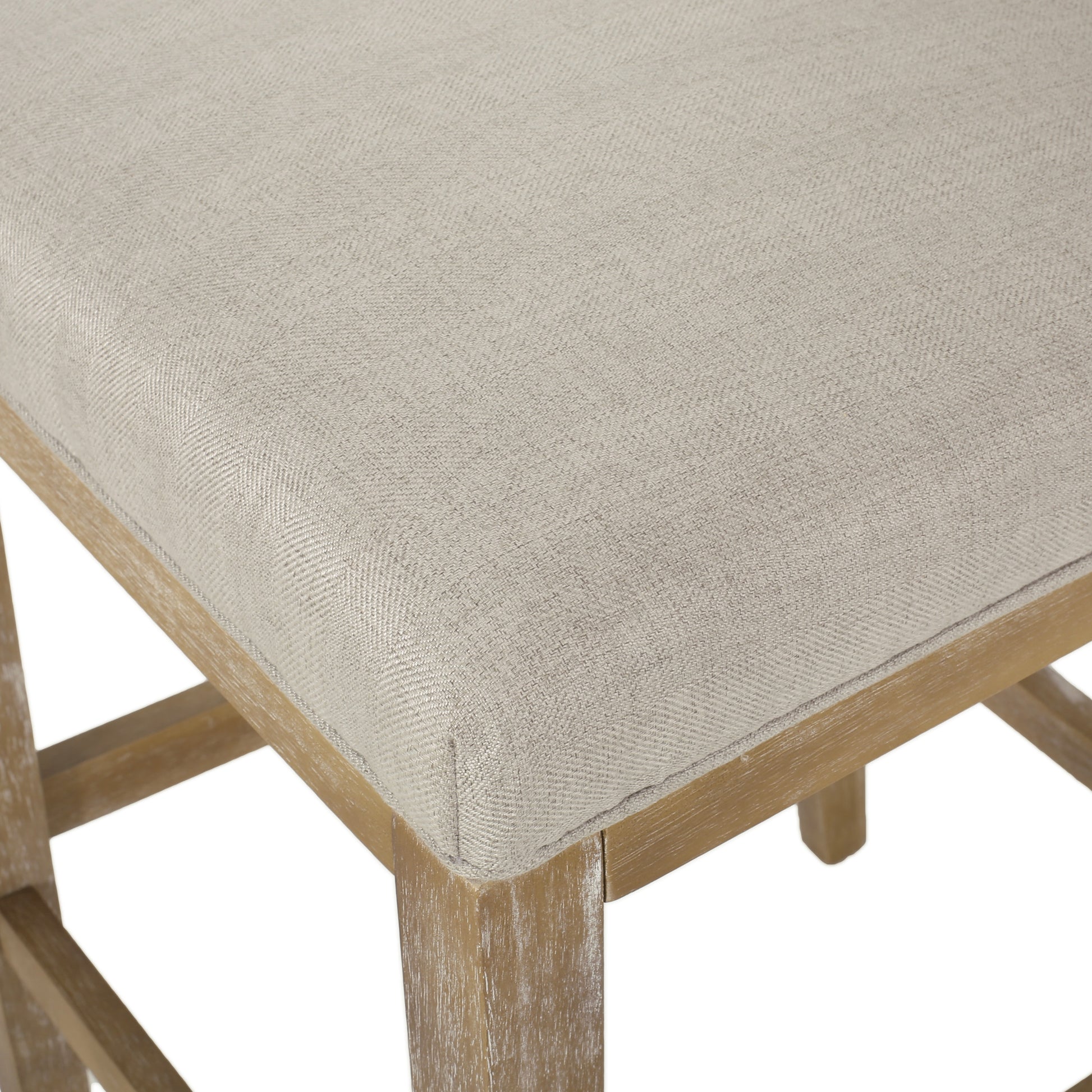 Closeup of a light beige upholstered bar stool seat with a subtle herringbone texture on a distressed wood frame
