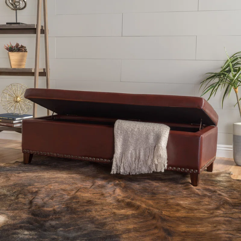 Brown leather storage ottoman with tufted nailhead trim and open lid revealing blanket