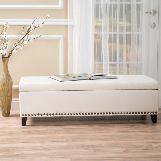 Cream upholstered storage bench with decorative nailhead trim and open book