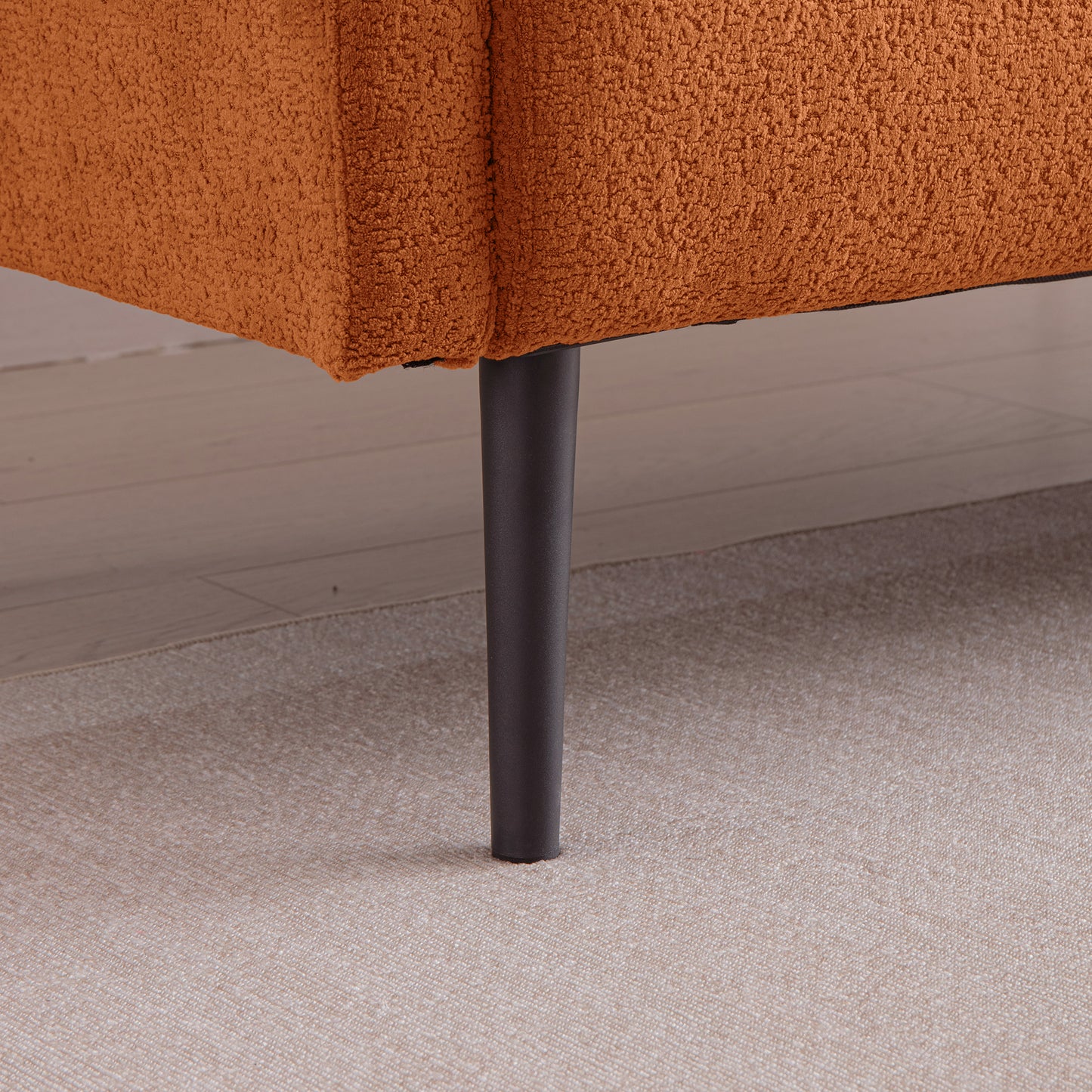 Closeup of orange boucl sofa fabric texture with dark metal tapered leg
