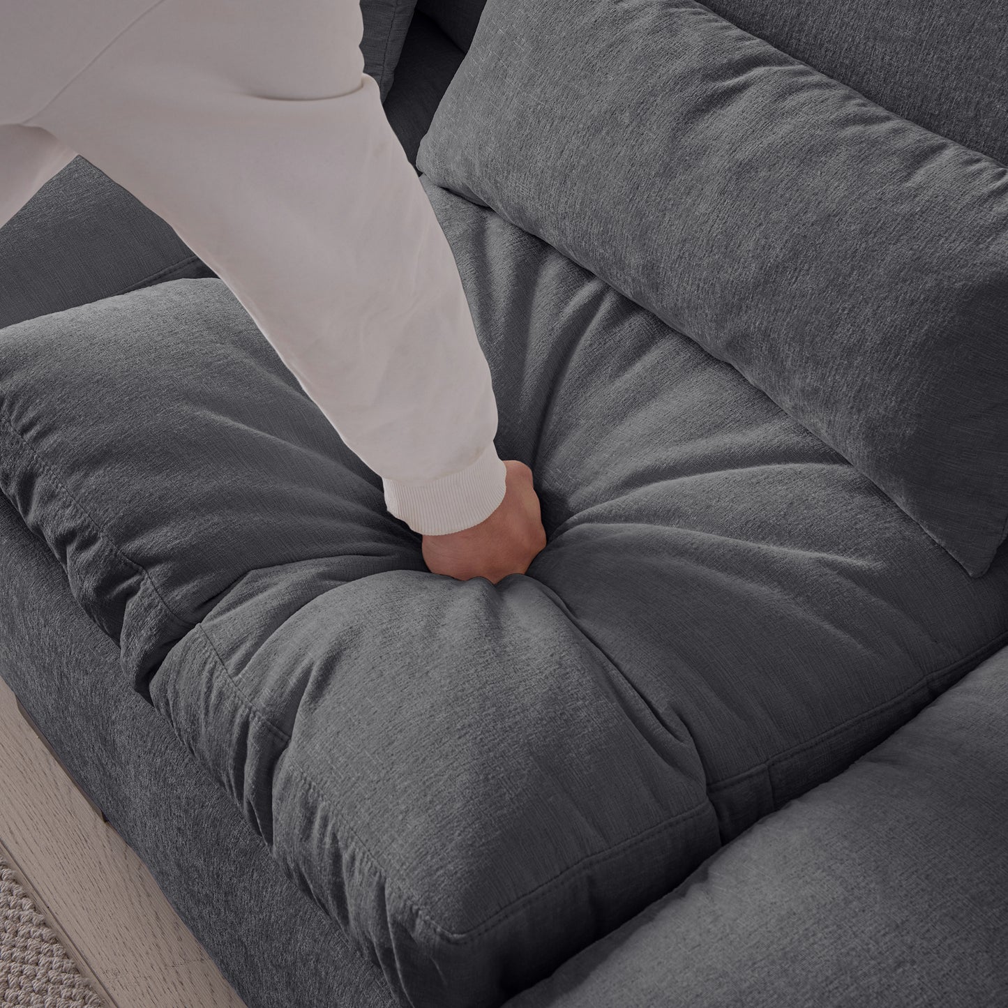 Hand pressing into plush gray fabric sofa cushion for comfort demonstration