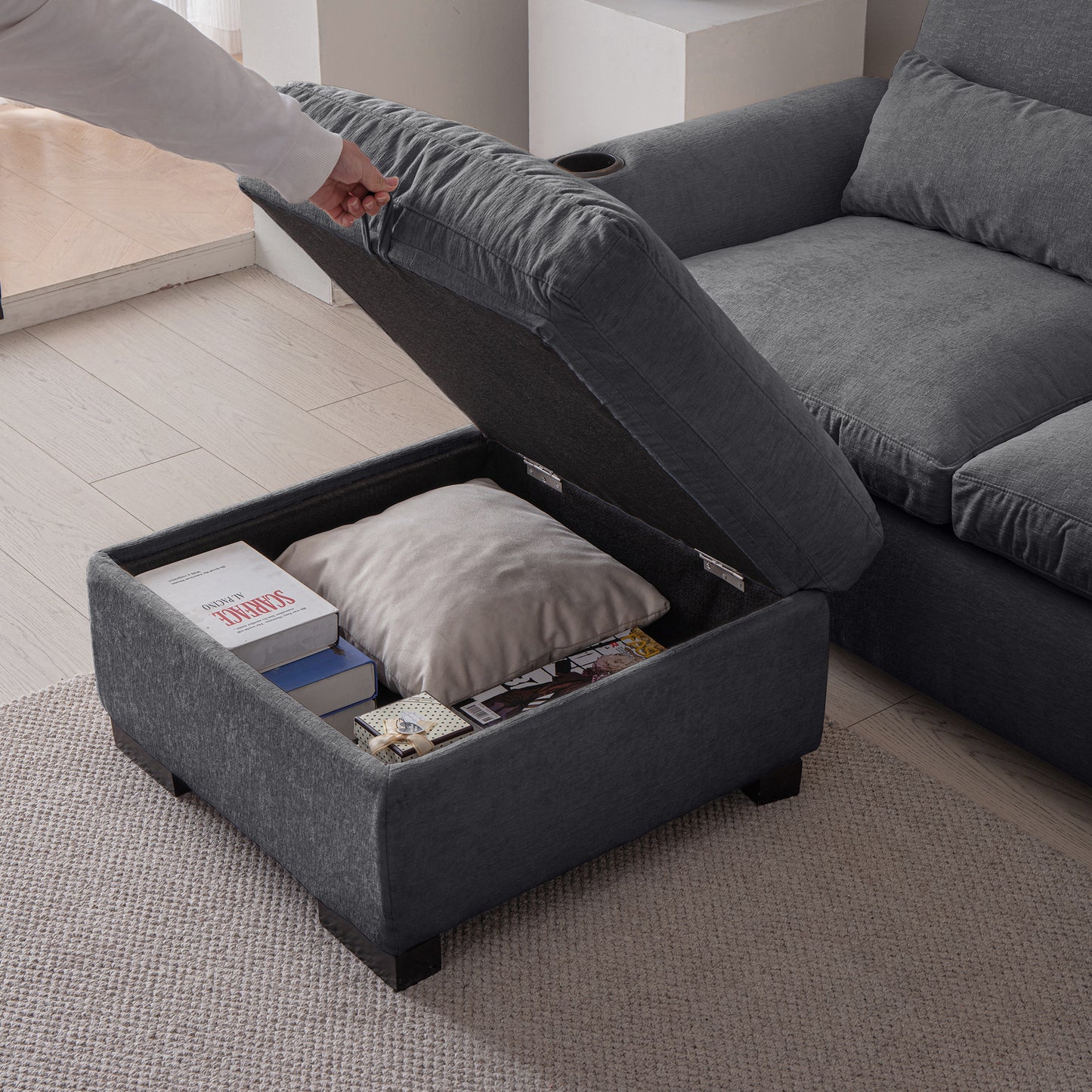 Dark grey fabric ottoman with open storage compartment revealing books pillow and magazine for living room storage