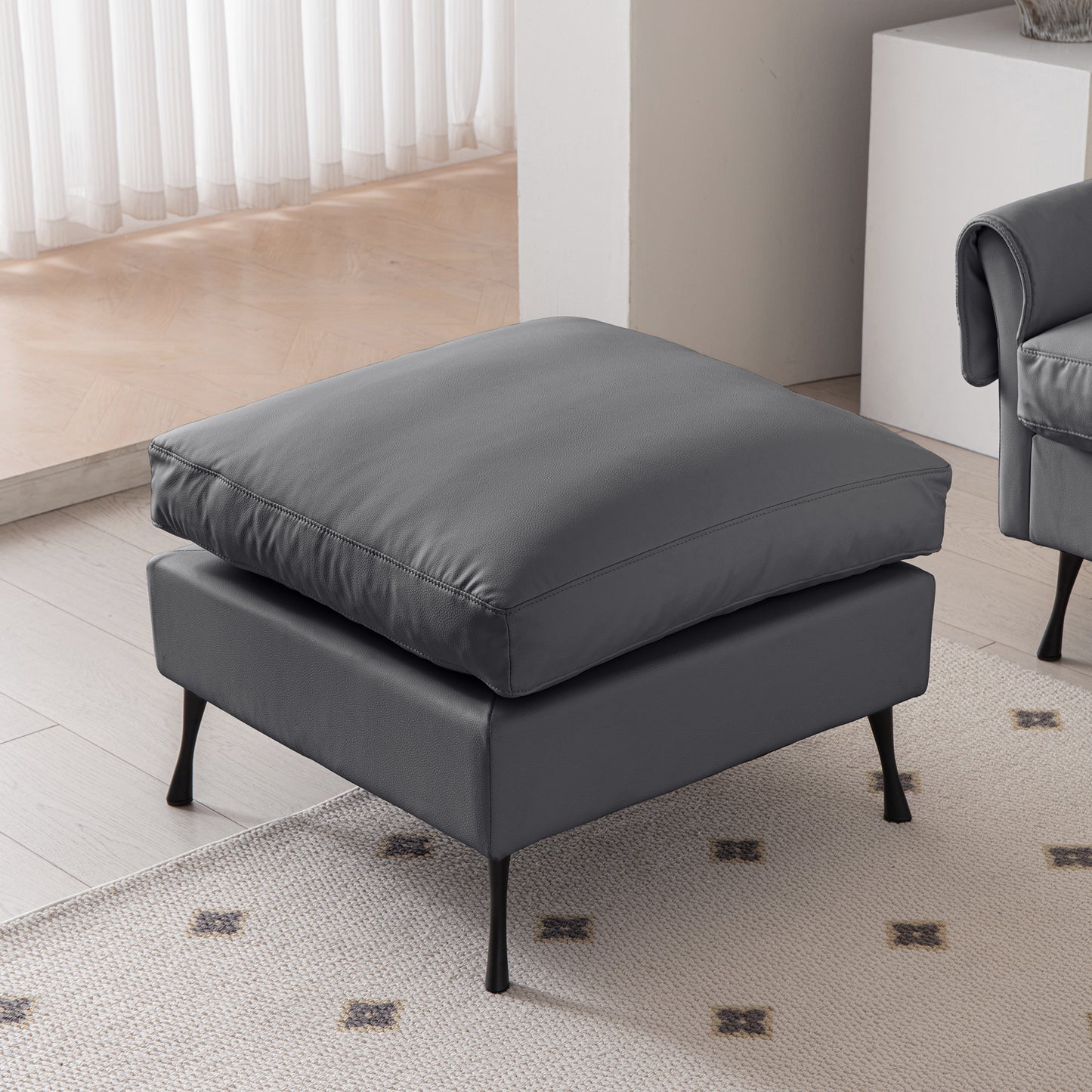 Modern charcoal grey leather ottoman with plush cushioning and sleek metal legs