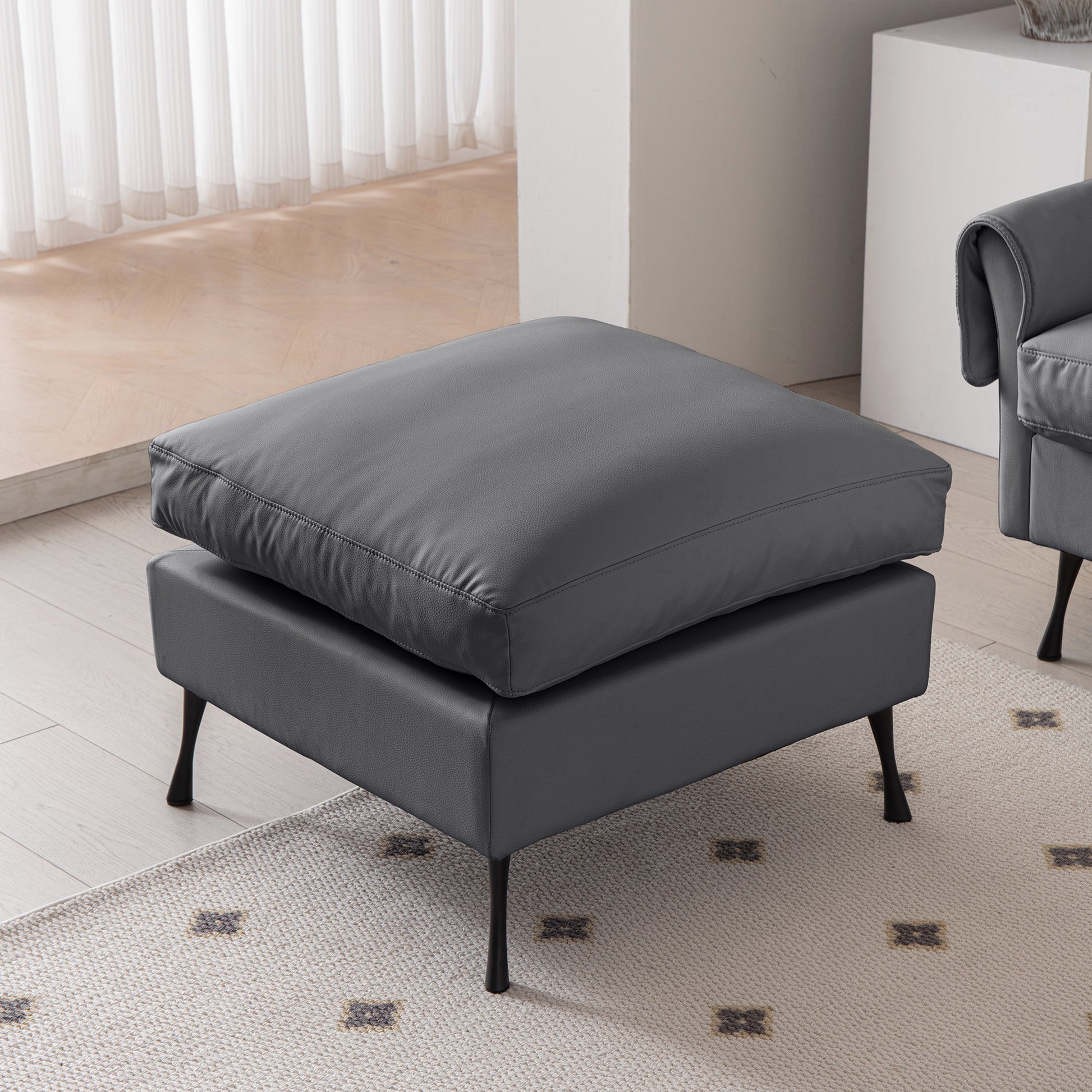 Modern charcoal grey leather ottoman with plush cushioning and sleek metal legs