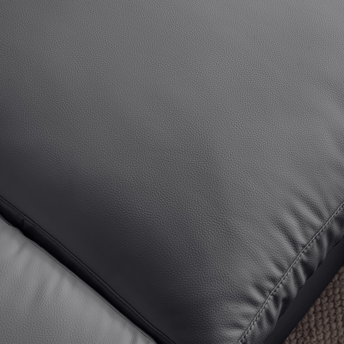 Closeup texture of a charcoal grey faux leather sofa cushion with detailed stitching