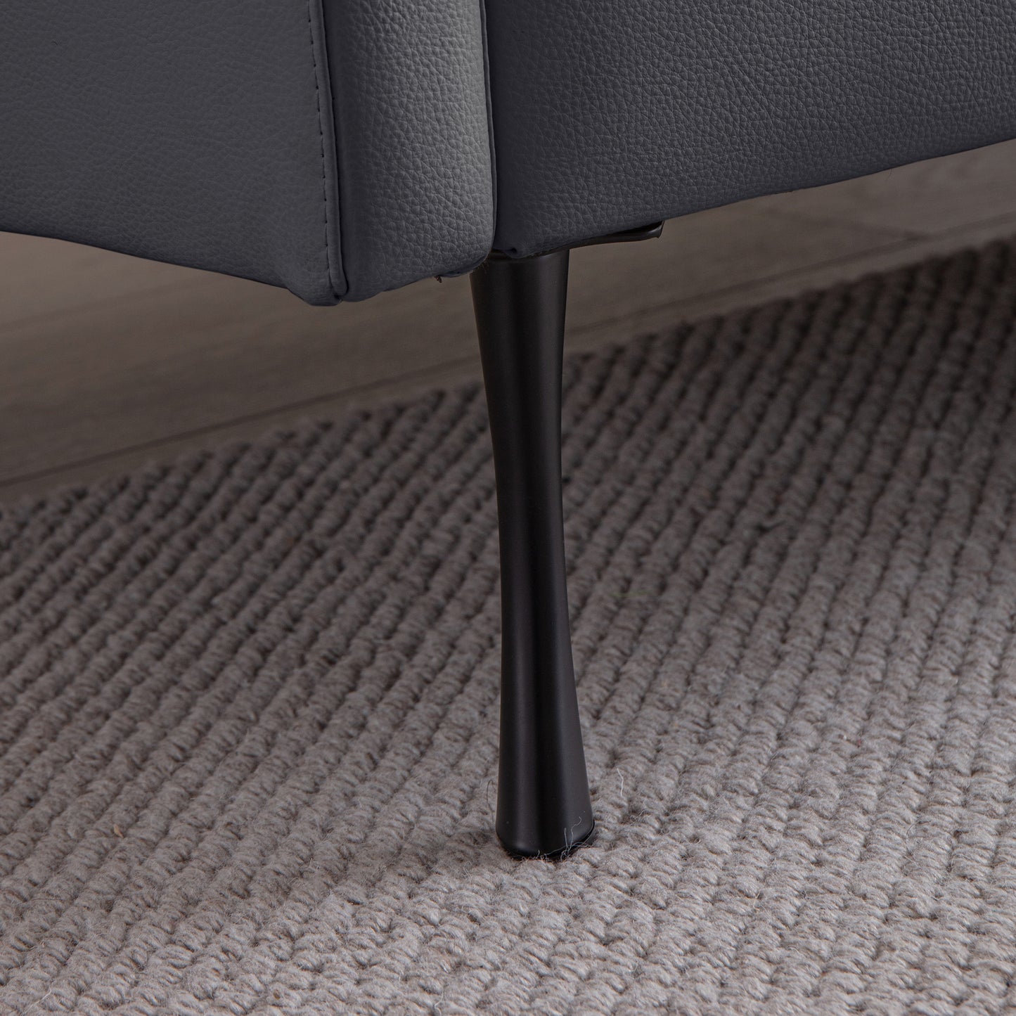 Close up of dark gray faux leather sofa armrest with black tapered metal leg