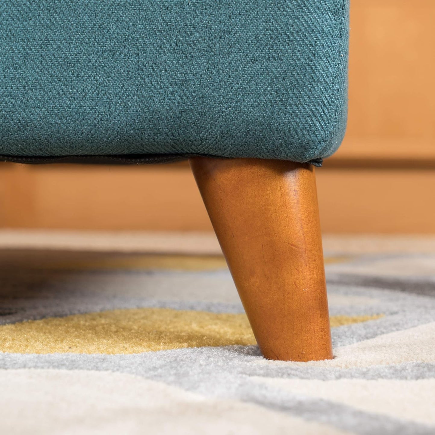 Close up of teal textured fabric on a sofa leg with a tapered wooden base on a patterned rug