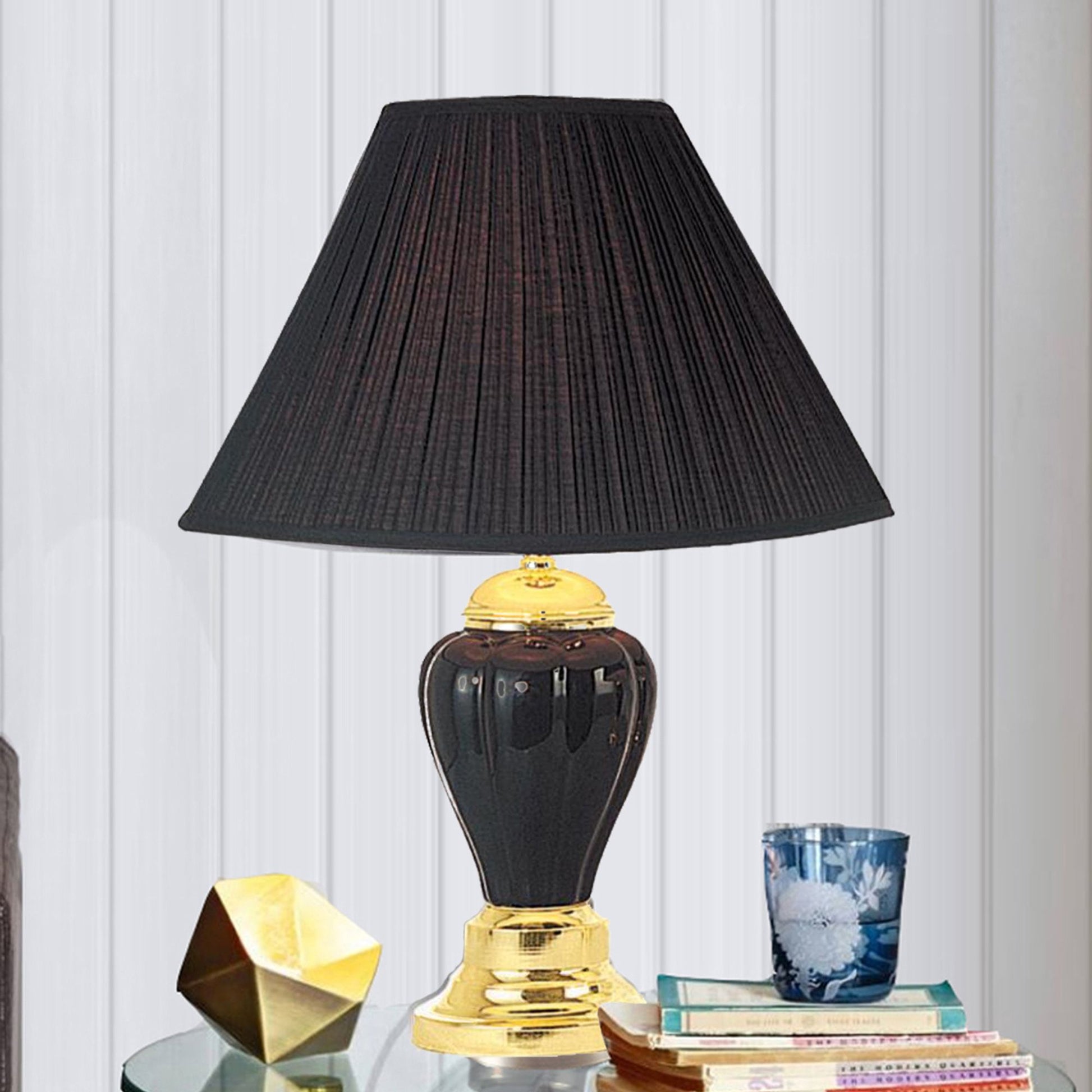Black pleated lampshade atop a glossy black ceramic table lamp with gold accents
