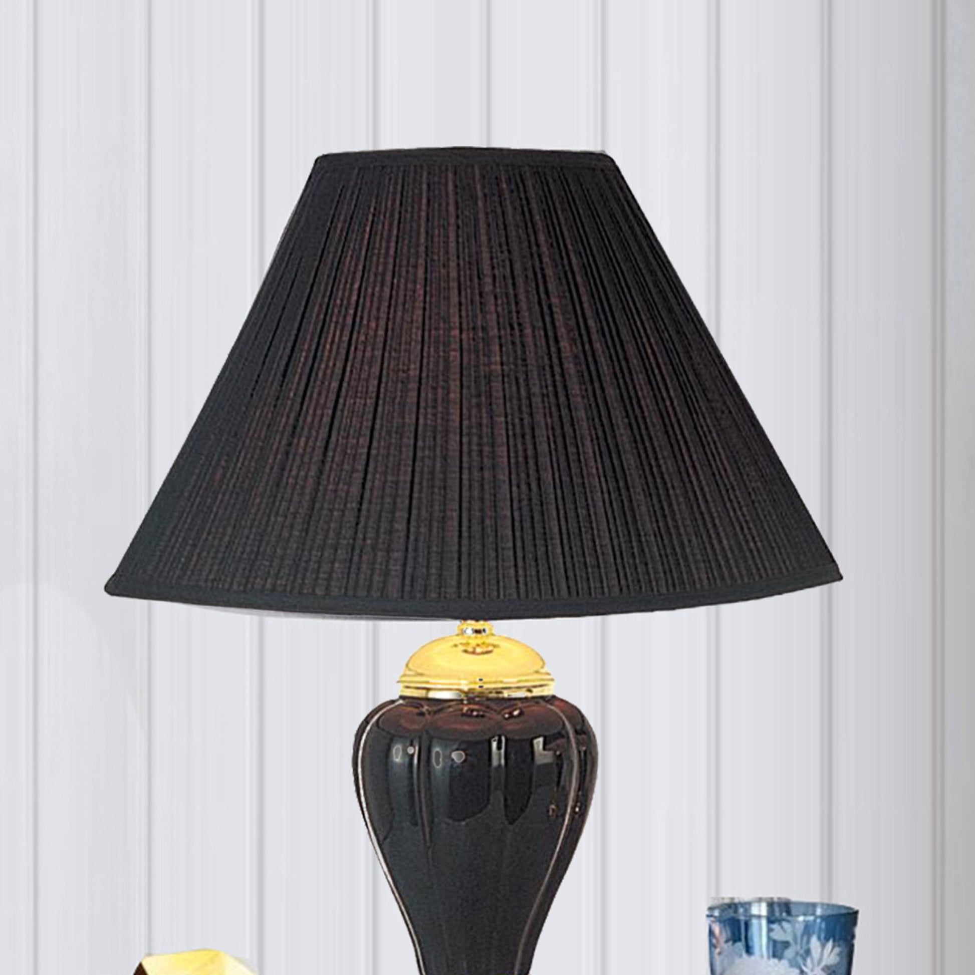 Pleated black lampshade with a gold finial on a dark ceramic base