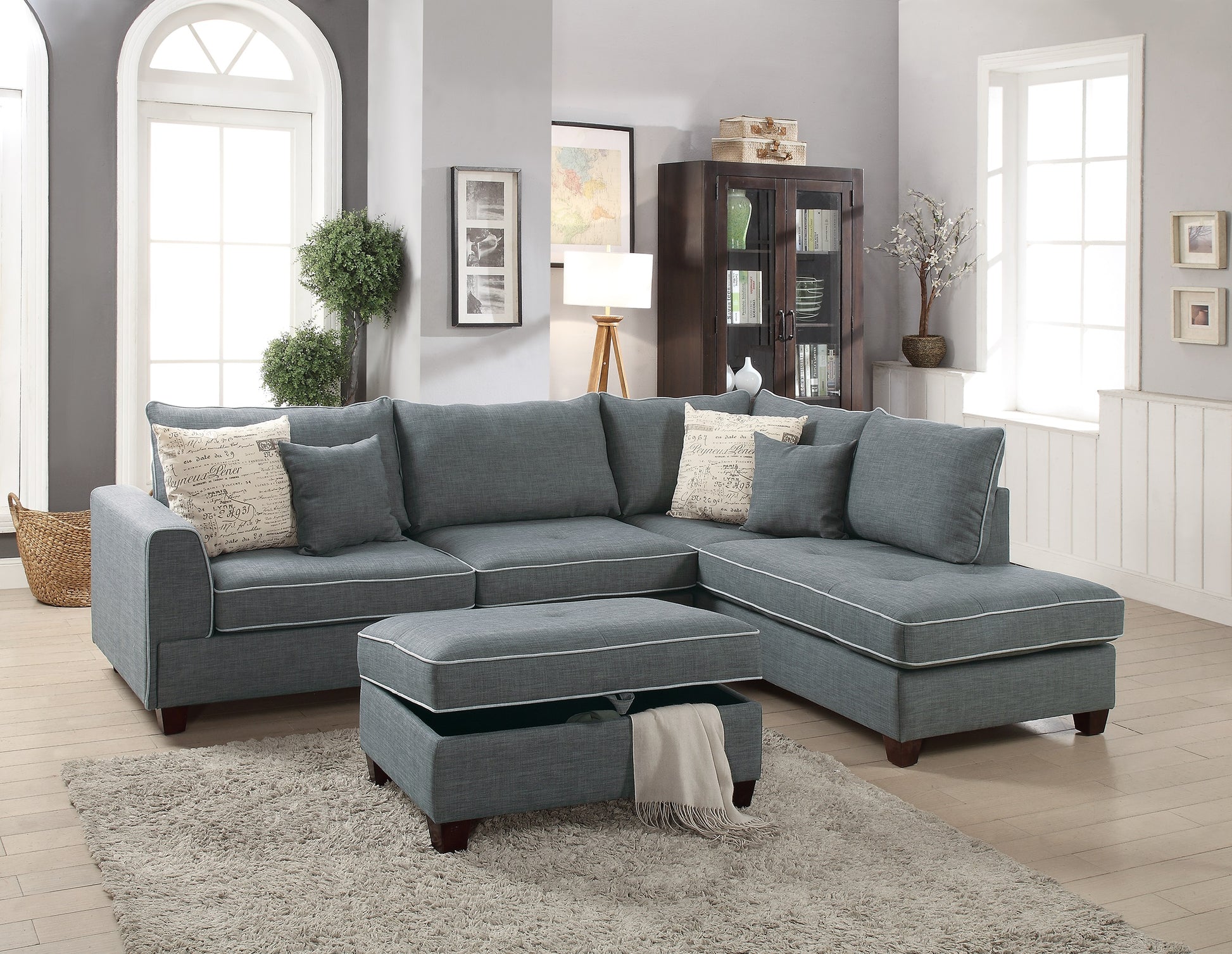 Gray sectional sofa with chaise and storage ottoman featuring white piping and accent pillows