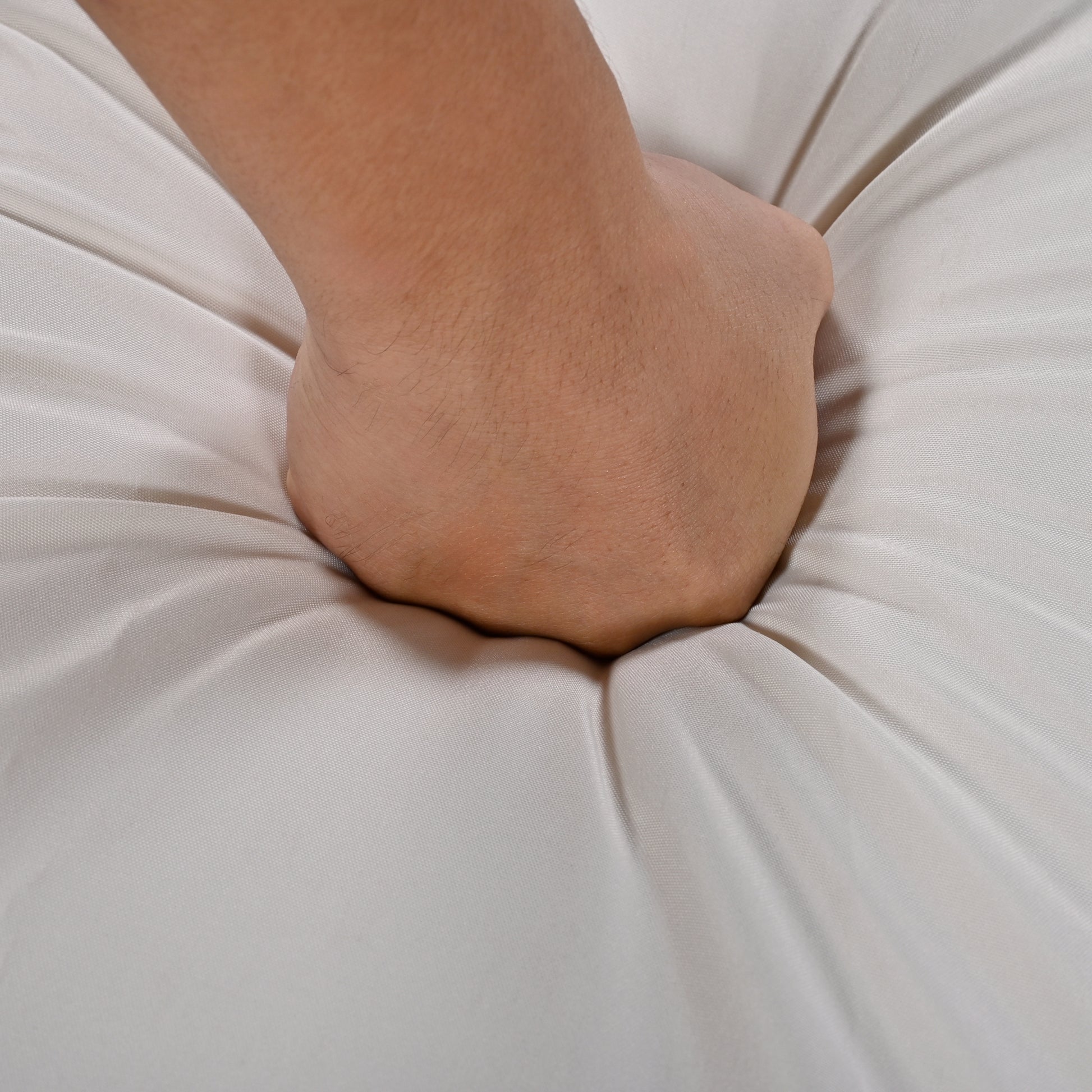 Hand pressing into plush beige mattress for comfort test