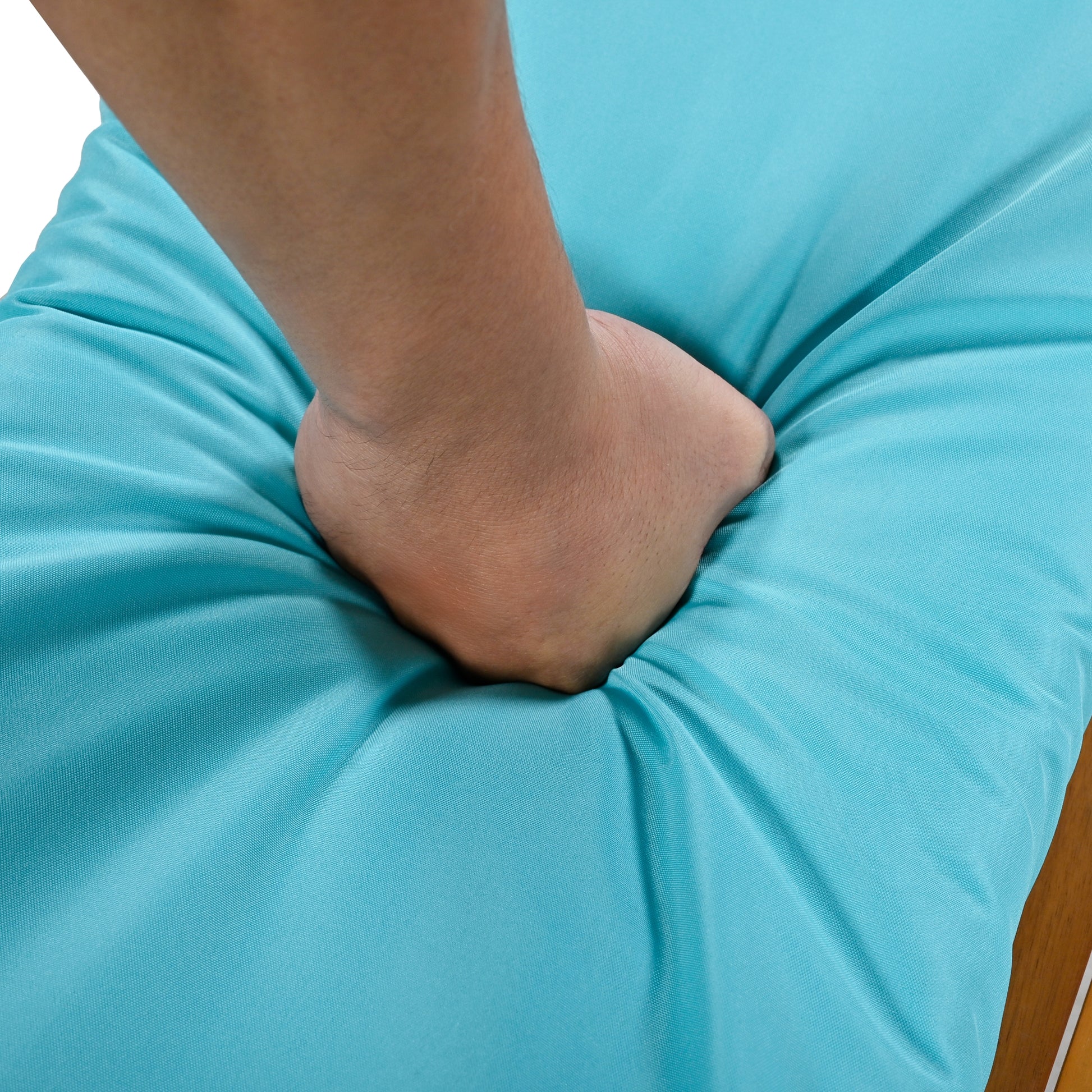 Closeup of a hand pressing into a plush turquoise outdoor cushion for comfort