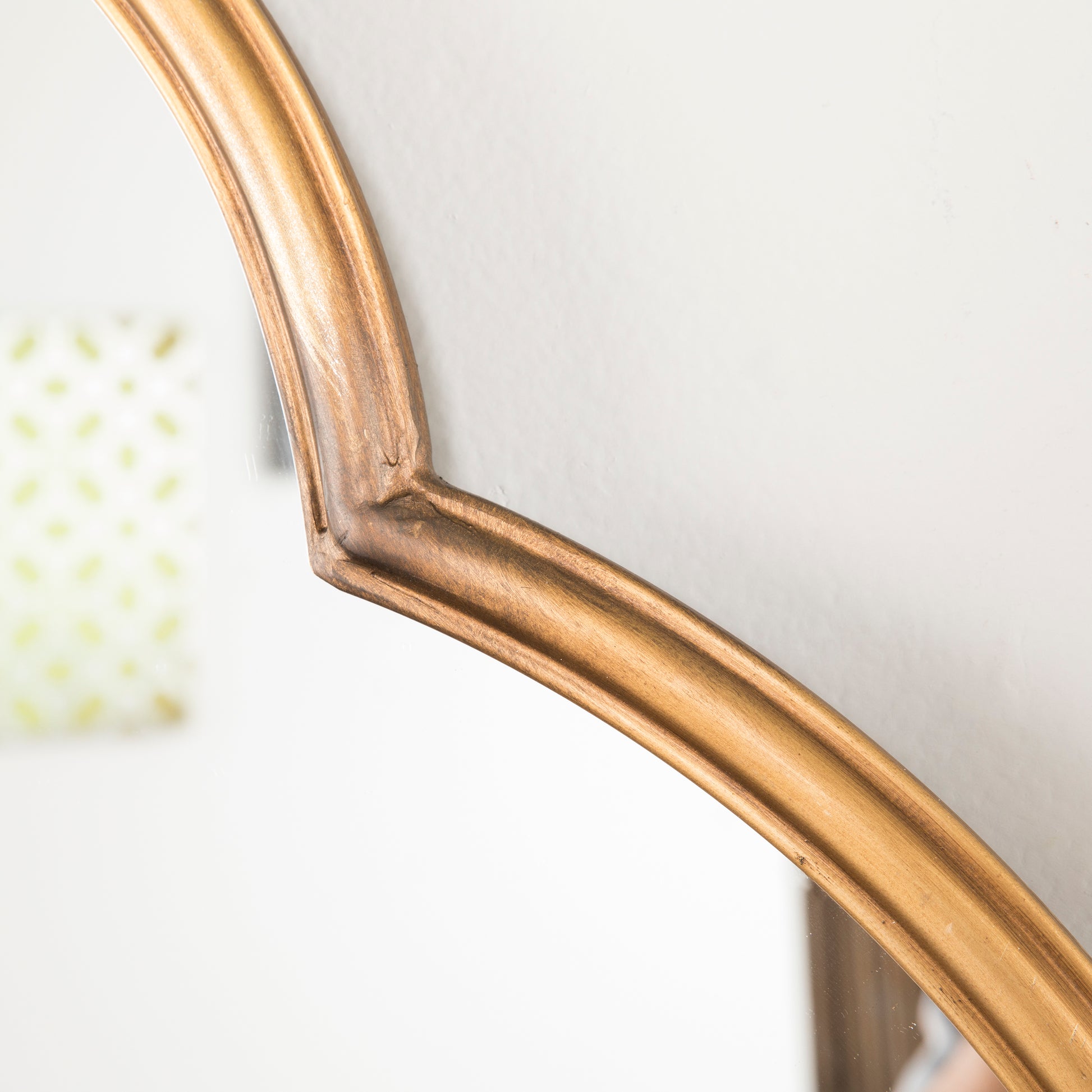 Antique gold ornate mirror frame with subtle wood grain texture reflecting a blurred patterned background
