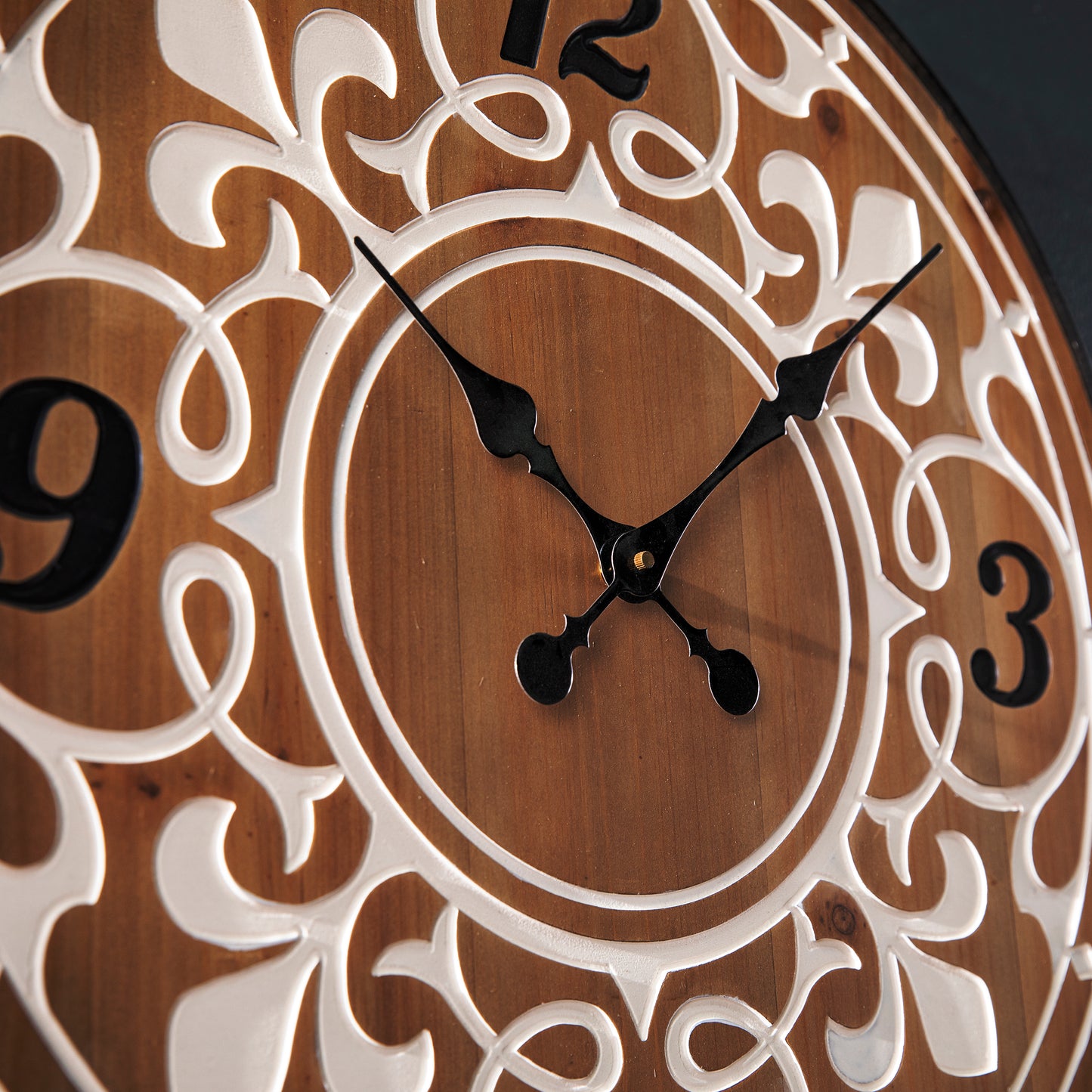 Closeup of a decorative wooden wall clock with ornate white scrollwork and black hands