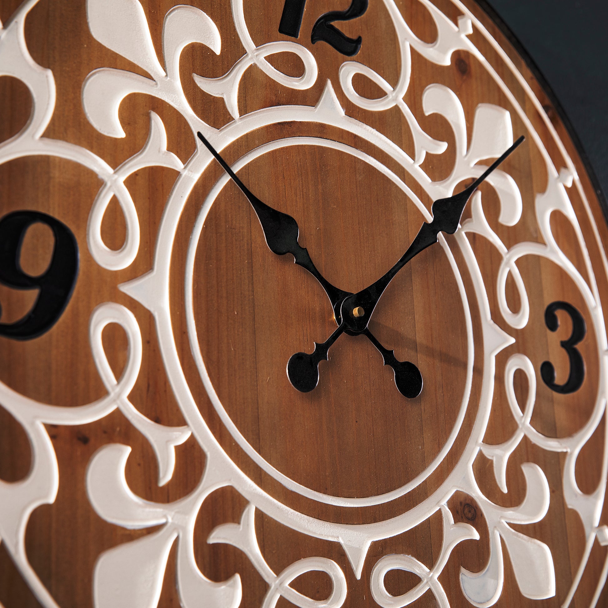 Closeup of a decorative wooden wall clock with ornate white scrollwork and black hands