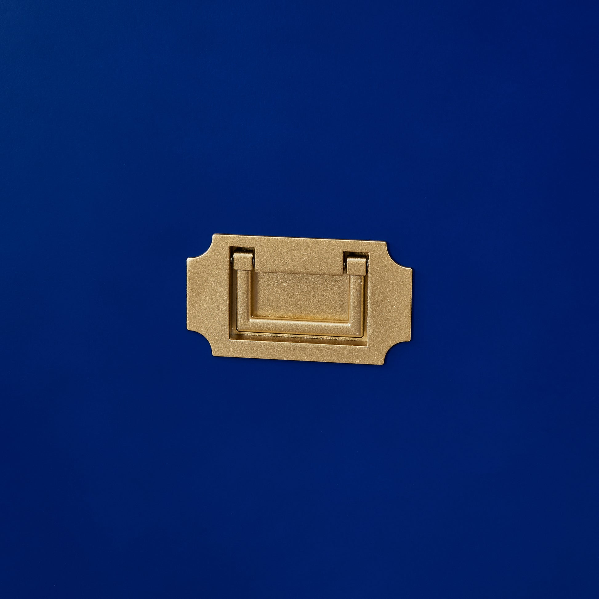 Brushed brass campaign handle with decorative backplate on navy blue surface