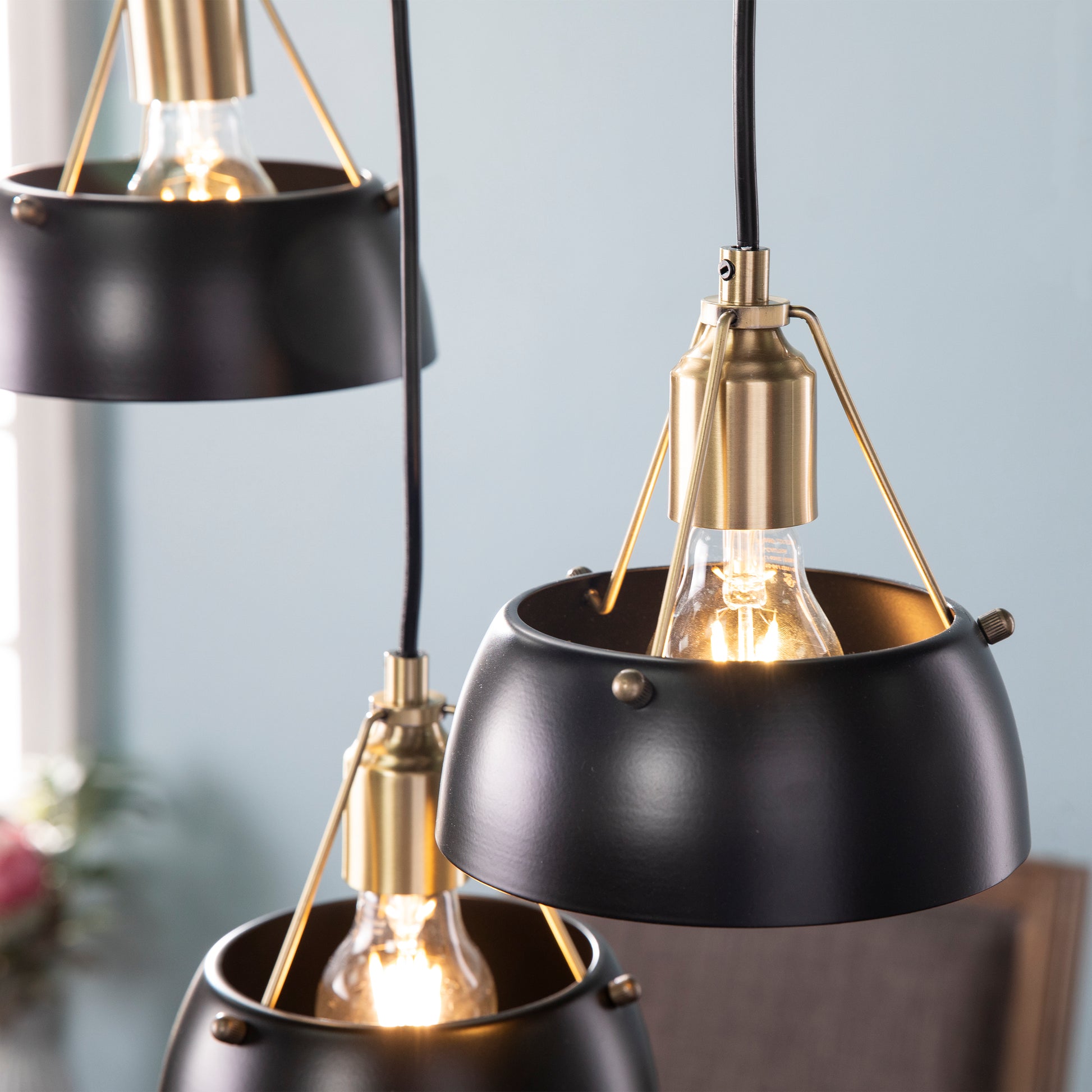 Closeup of three black pendant lights with brass accents and exposed Edison bulbs