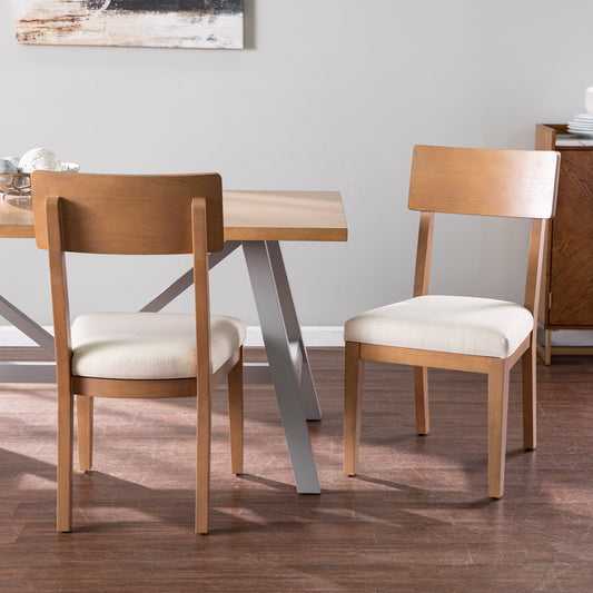 Two light oak dining chairs with cream upholstered seats sit beside a wooden dining table