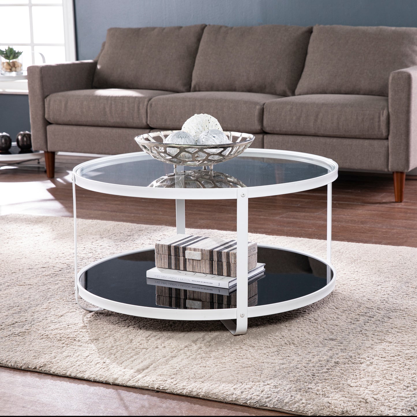 White round coffee table with glass top and lower shelf featuring decorative objects