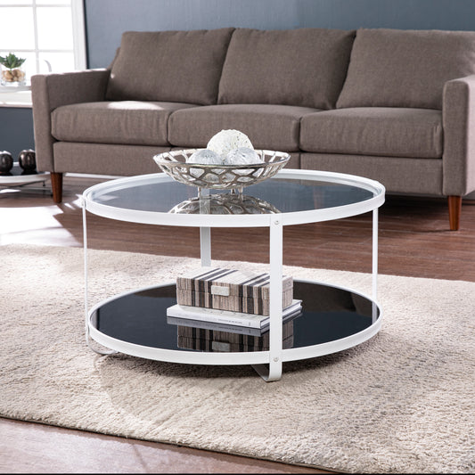 White round coffee table with glass top and lower shelf featuring decorative objects