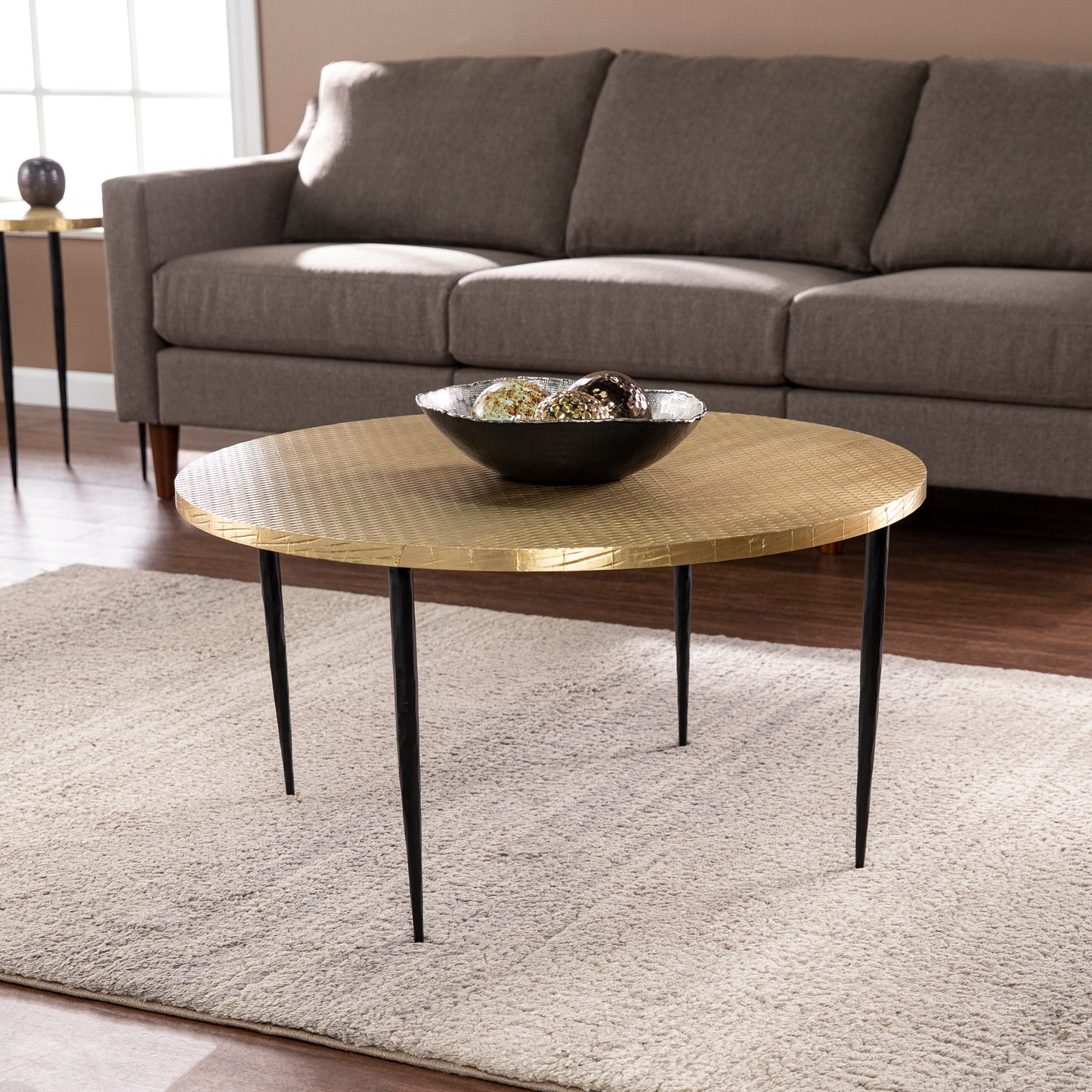 Round gold hammered coffee table with black metal legs and textured surface