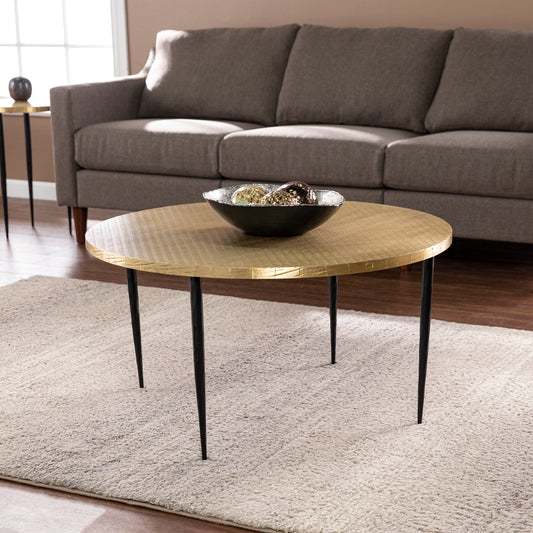 Round gold hammered coffee table with black metal legs and textured surface