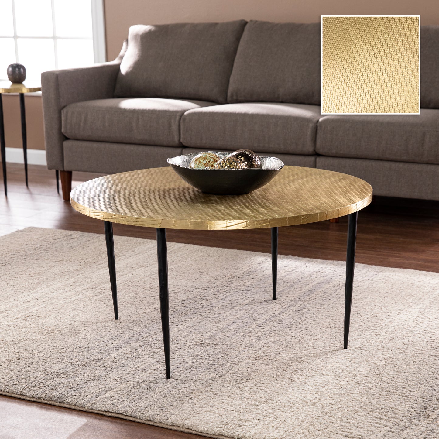 Round gold coffee table with black tapered legs and embossed geometric pattern