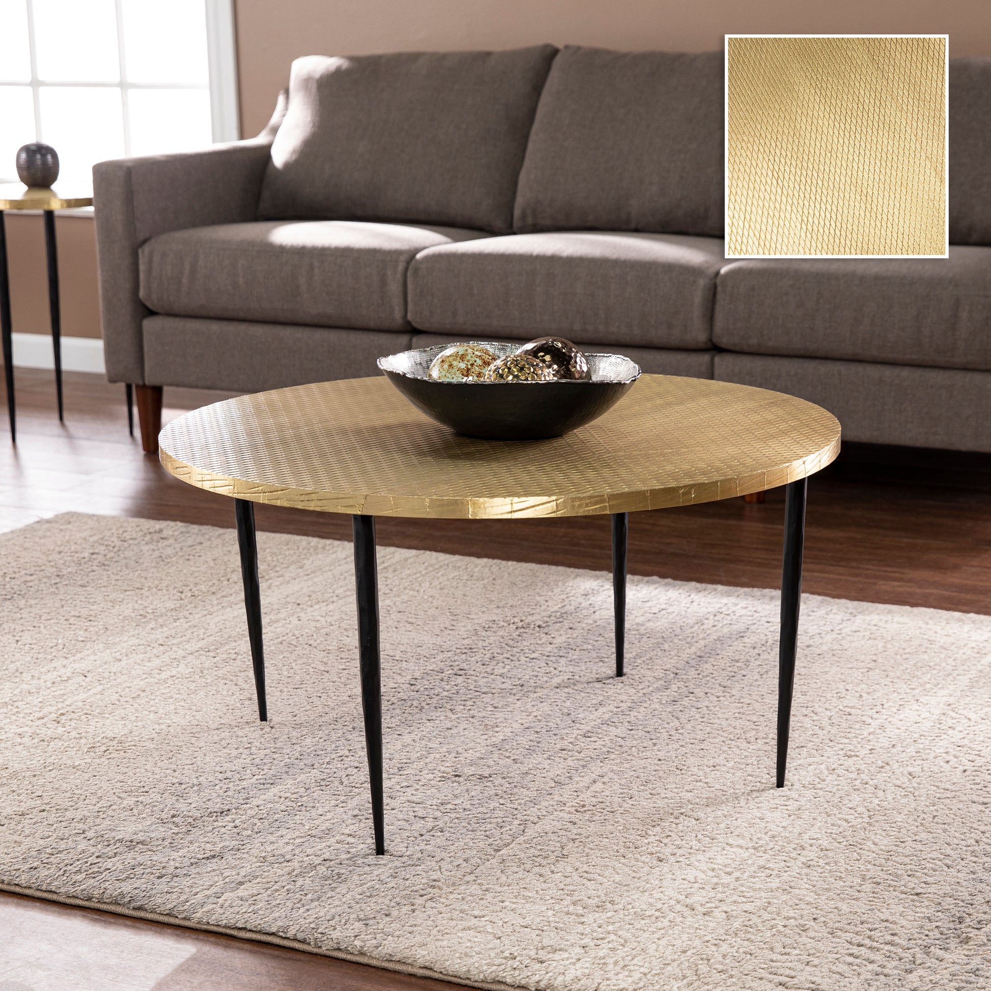 Round gold coffee table with black tapered legs and embossed geometric pattern
