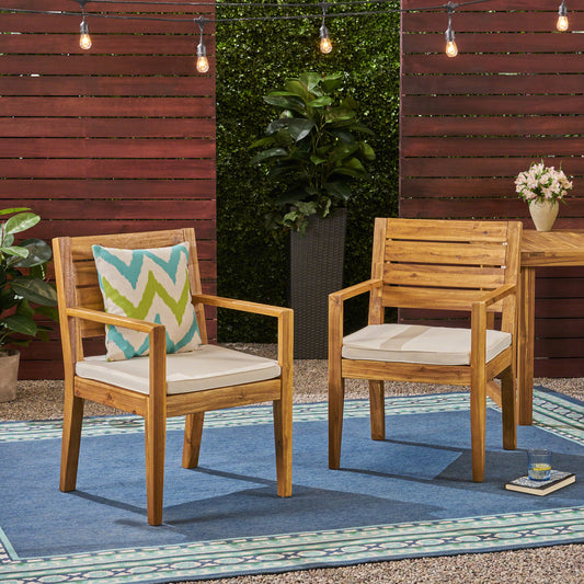 Two modern acacia wood patio chairs with cream cushions and a patterned accent pillow