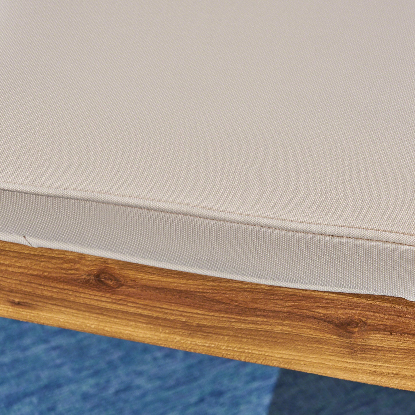 Closeup of a beige outdoor furniture cushion with visible texture on a wooden frame