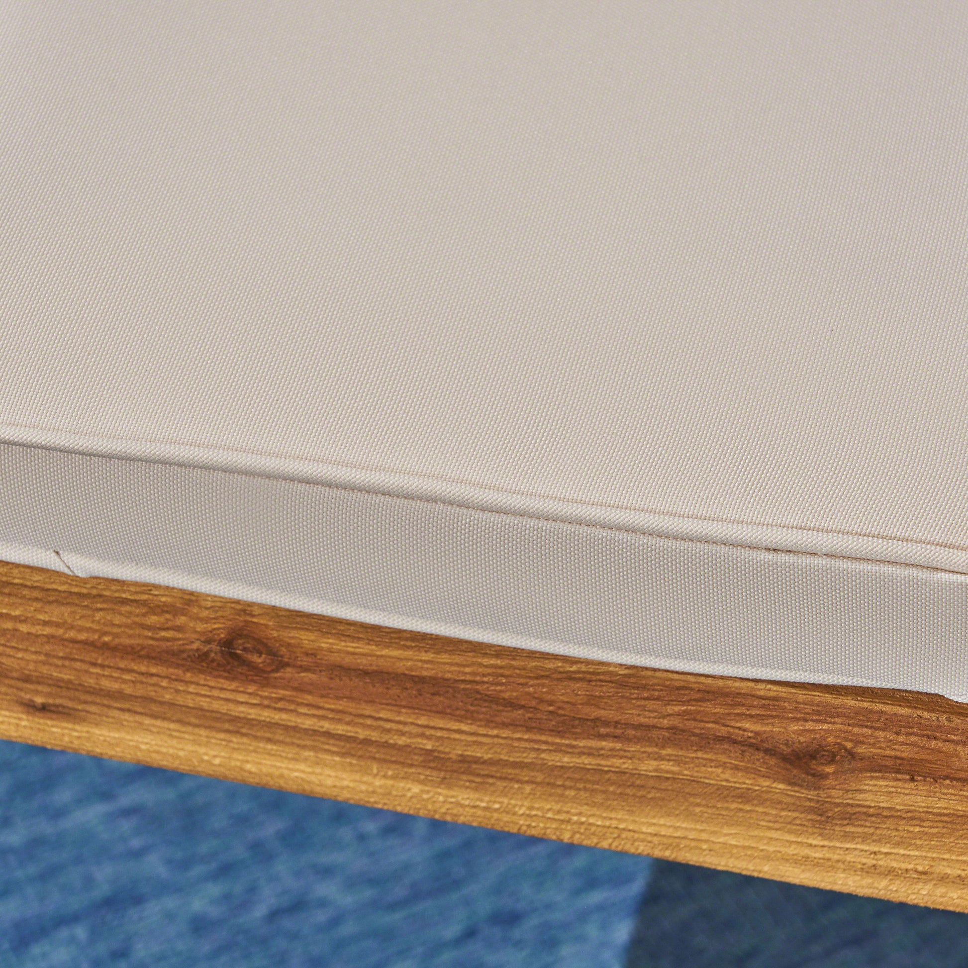 Closeup of a beige outdoor furniture cushion with visible texture on a wooden frame