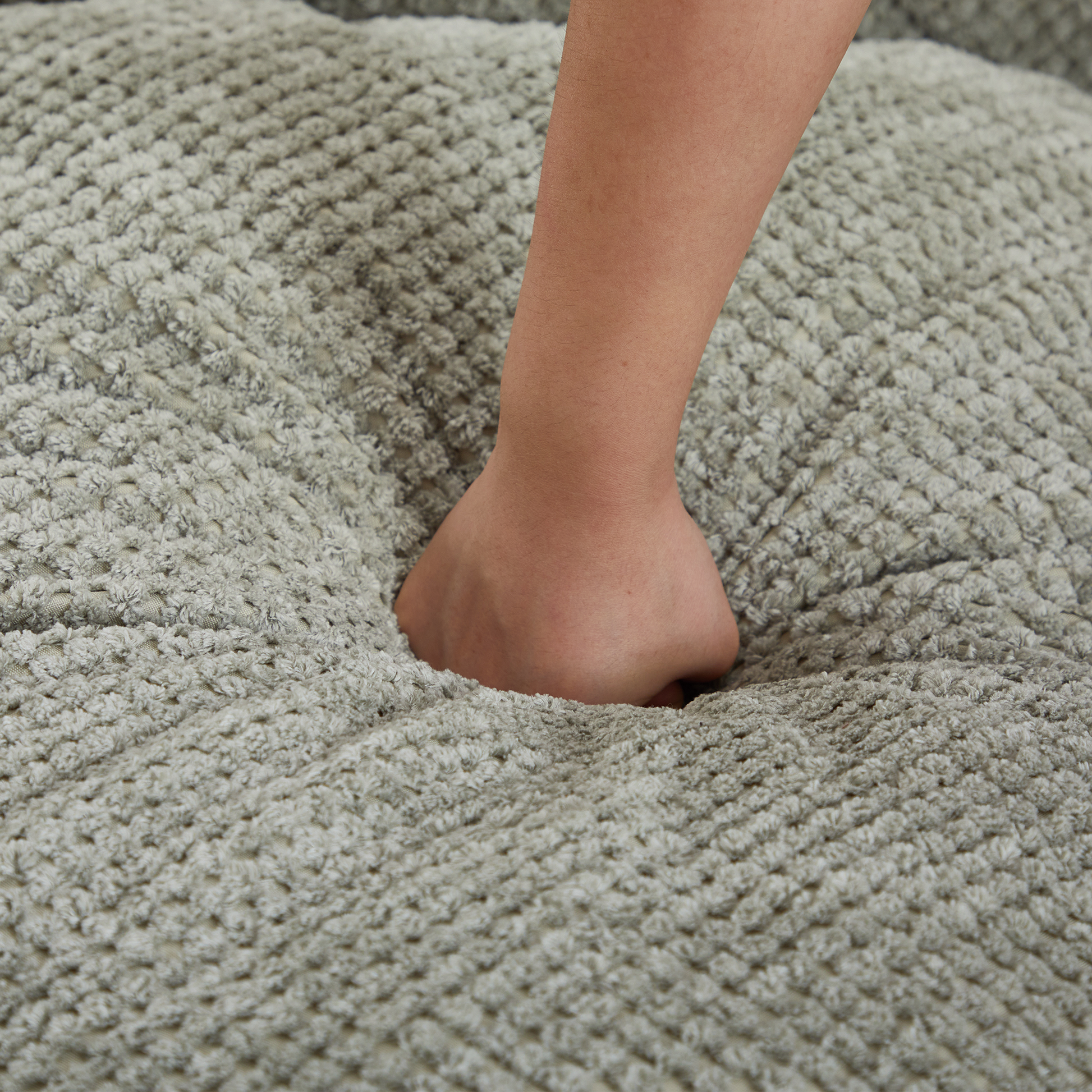 Closeup of a hand sinking into plush grey chenille fabric of a cozy throw pillow