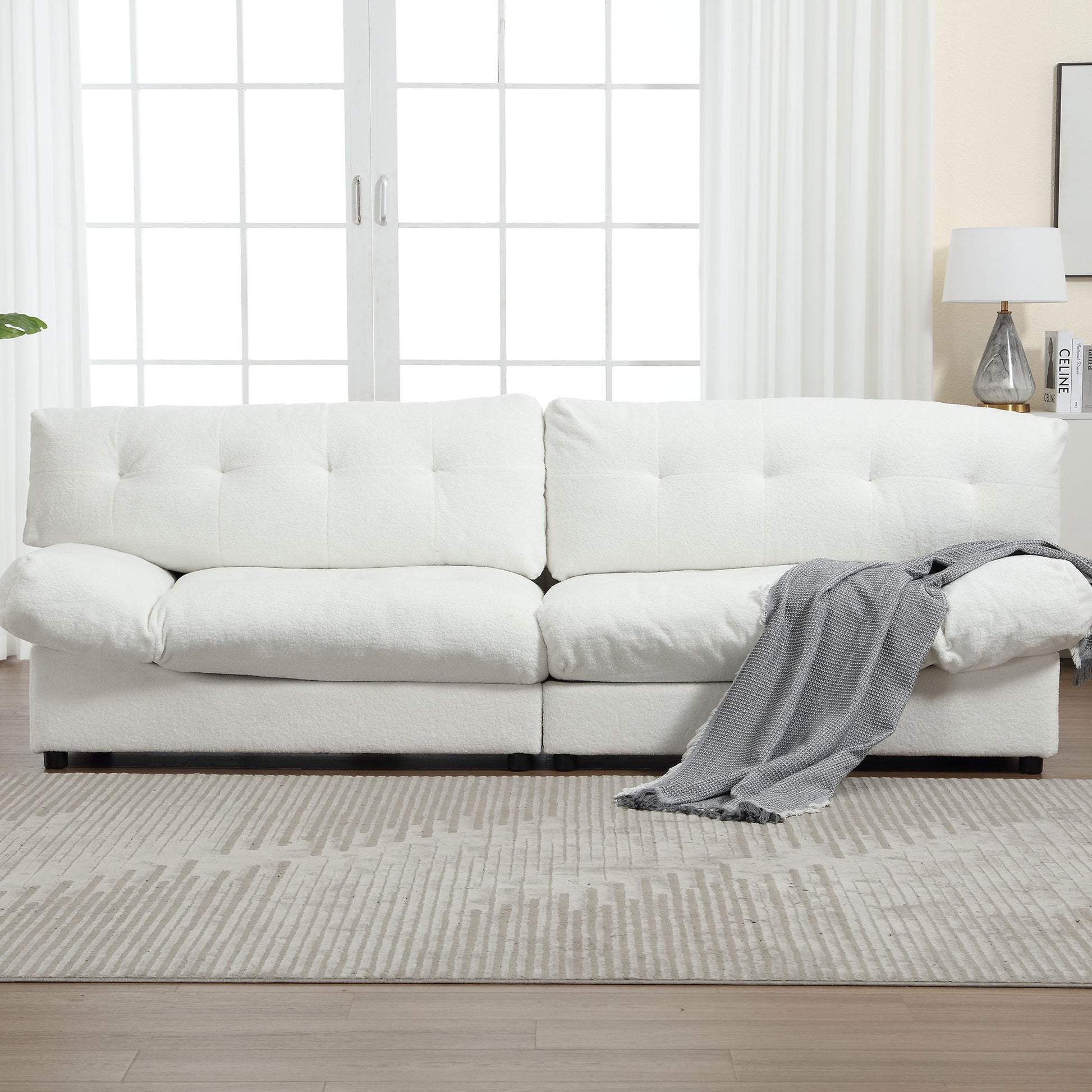 Plush white boucle fabric sofa with tufted back cushions and a grey throw blanket