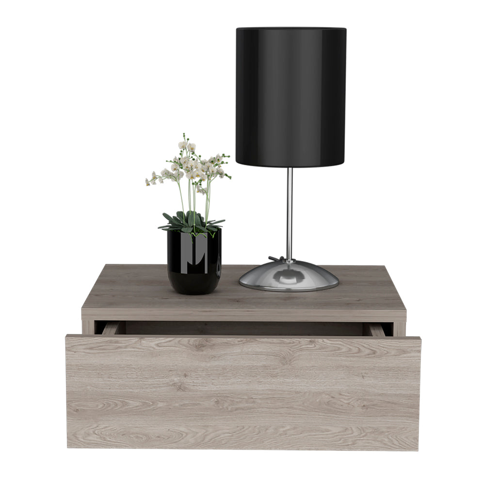 Modern grey wood bedside table with open drawer featuring a black lamp and potted white flowers