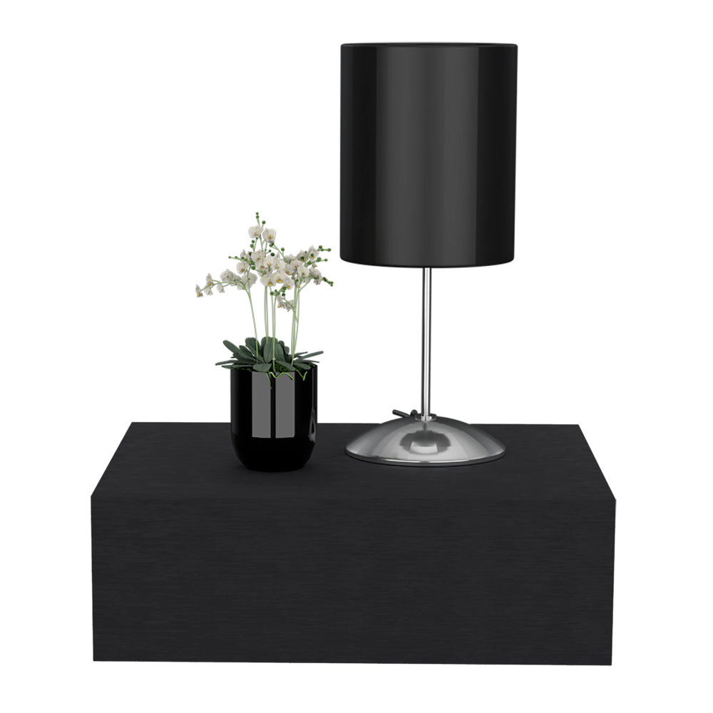 Sleek black cylinder table lamp with a polished metal base and a potted white orchid on a black floating shelf