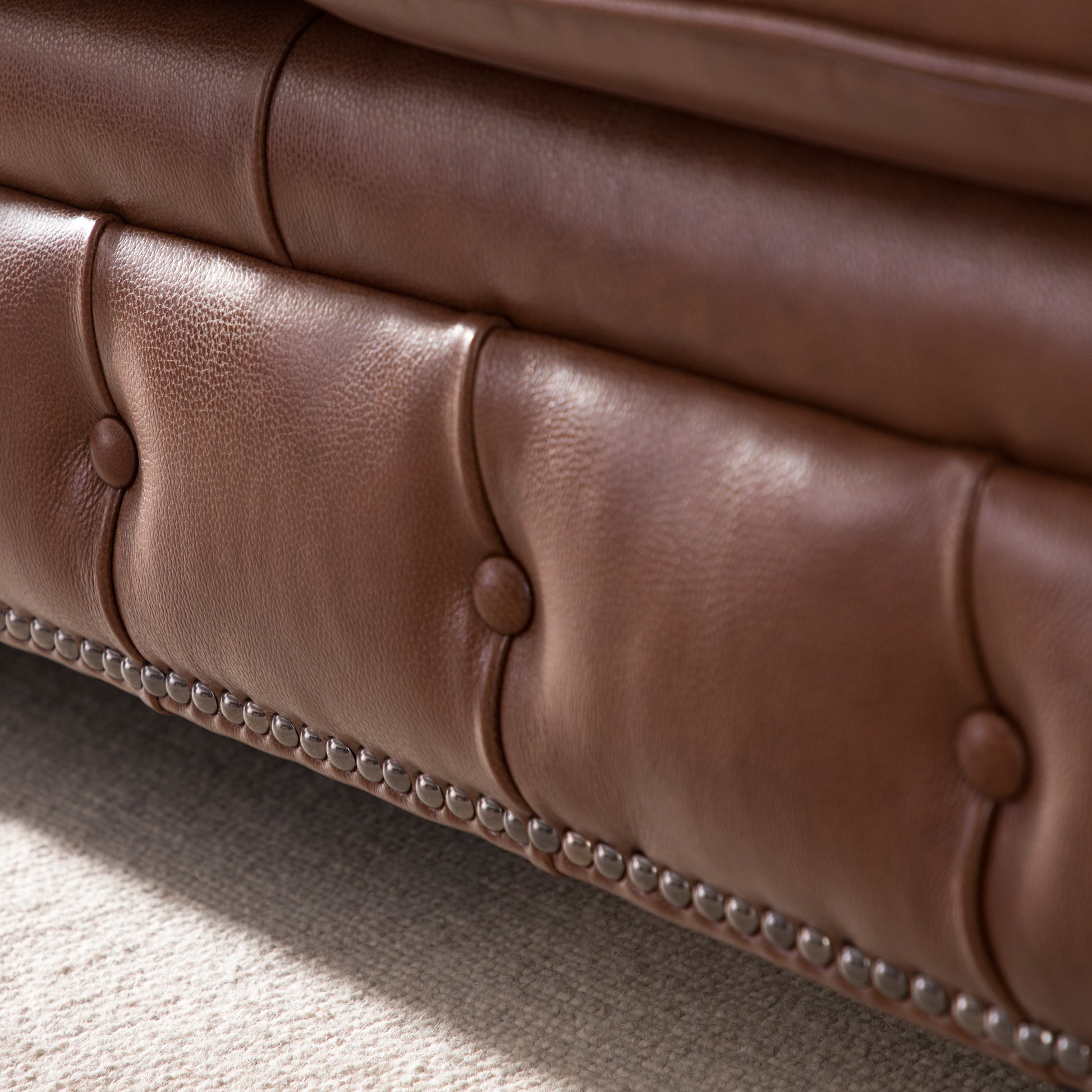 Brown leather tufted sofa detail with antique nailhead trim showcasing craftsmanship